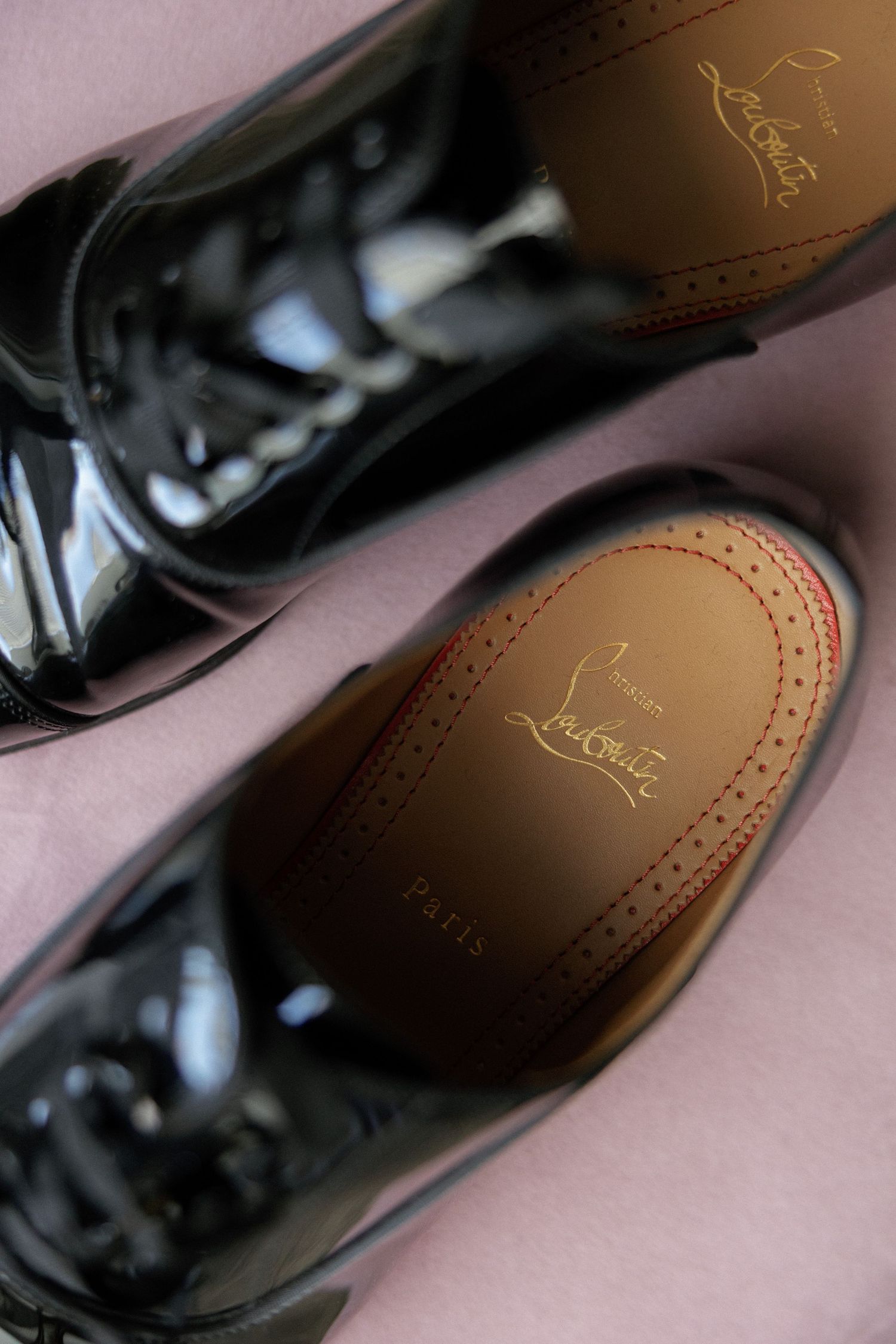 Black patent leather Christian Louboutin brogue oxford shoes showing signature red sole with gold logo detail.