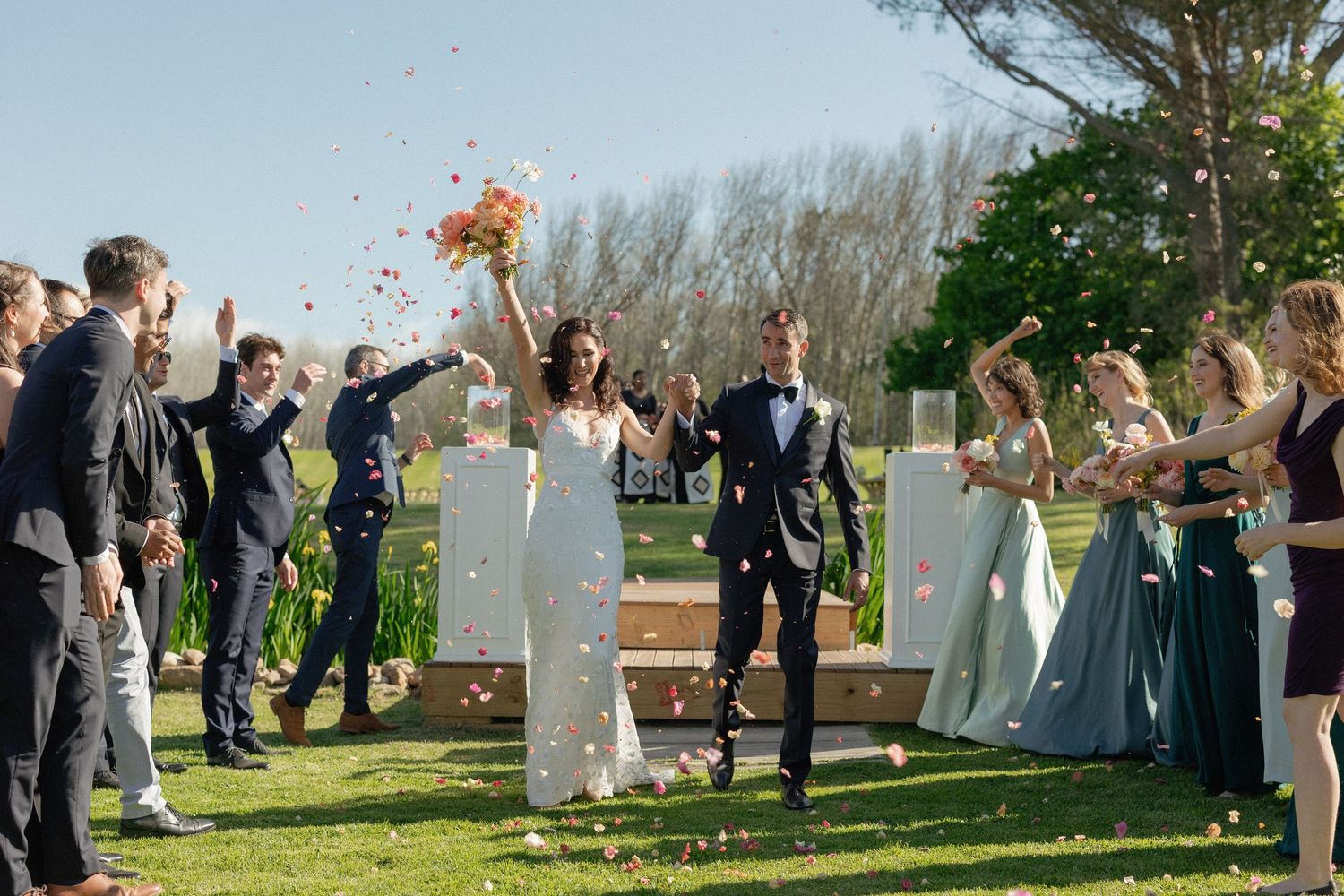 Bride and groom celebrated with confetti toss by guests during outdoor wedding ceremony exit.