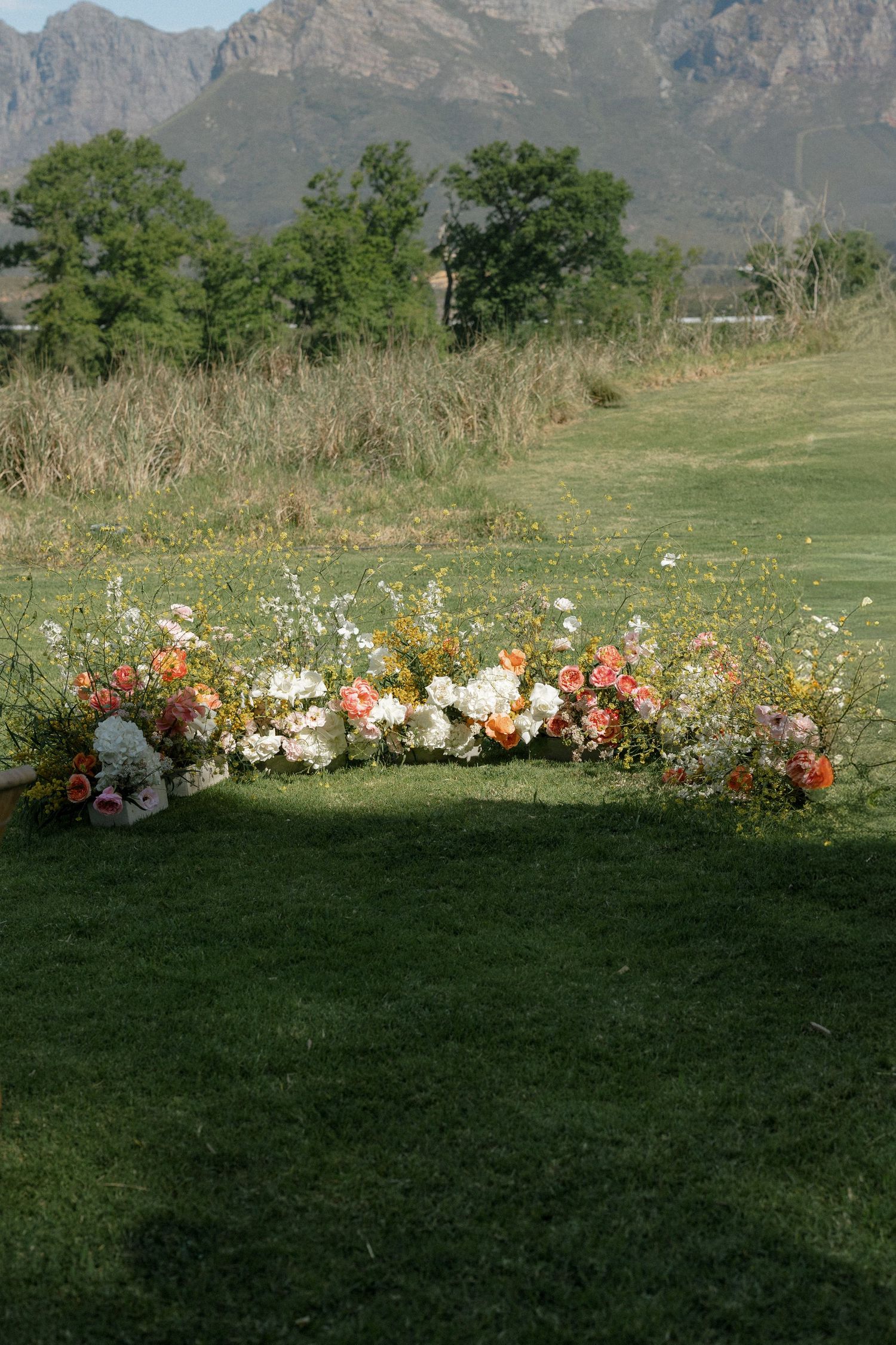 Colorful wedding ceremony floral arrangement with pink, white and orange blooms on green lawn with mountain backdrop.