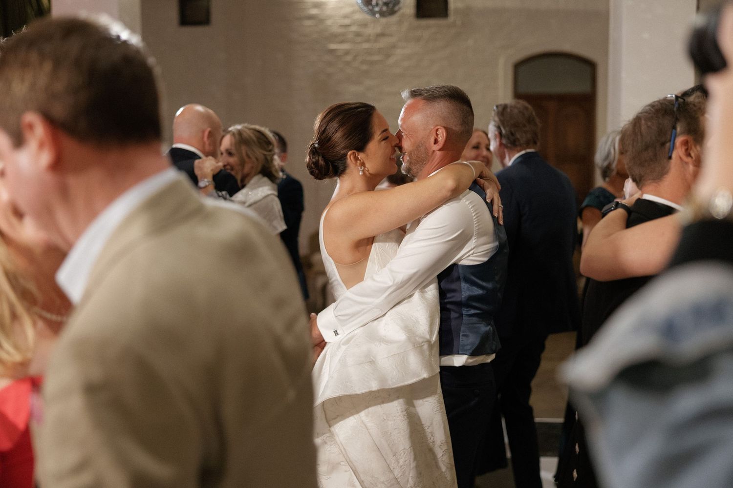 Bride and groom share first dance kiss at wedding reception surrounded by guests.