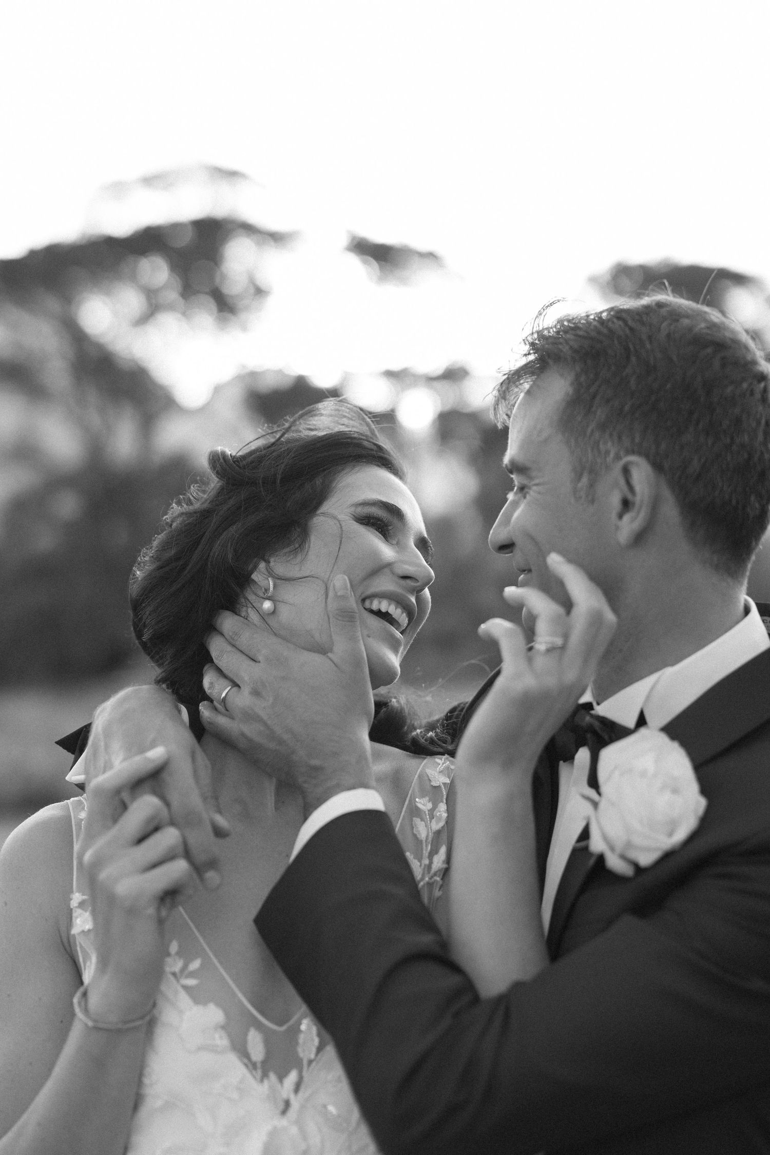 Black and white photo of laughing bride and groom sharing a joyful moment on their wedding day.