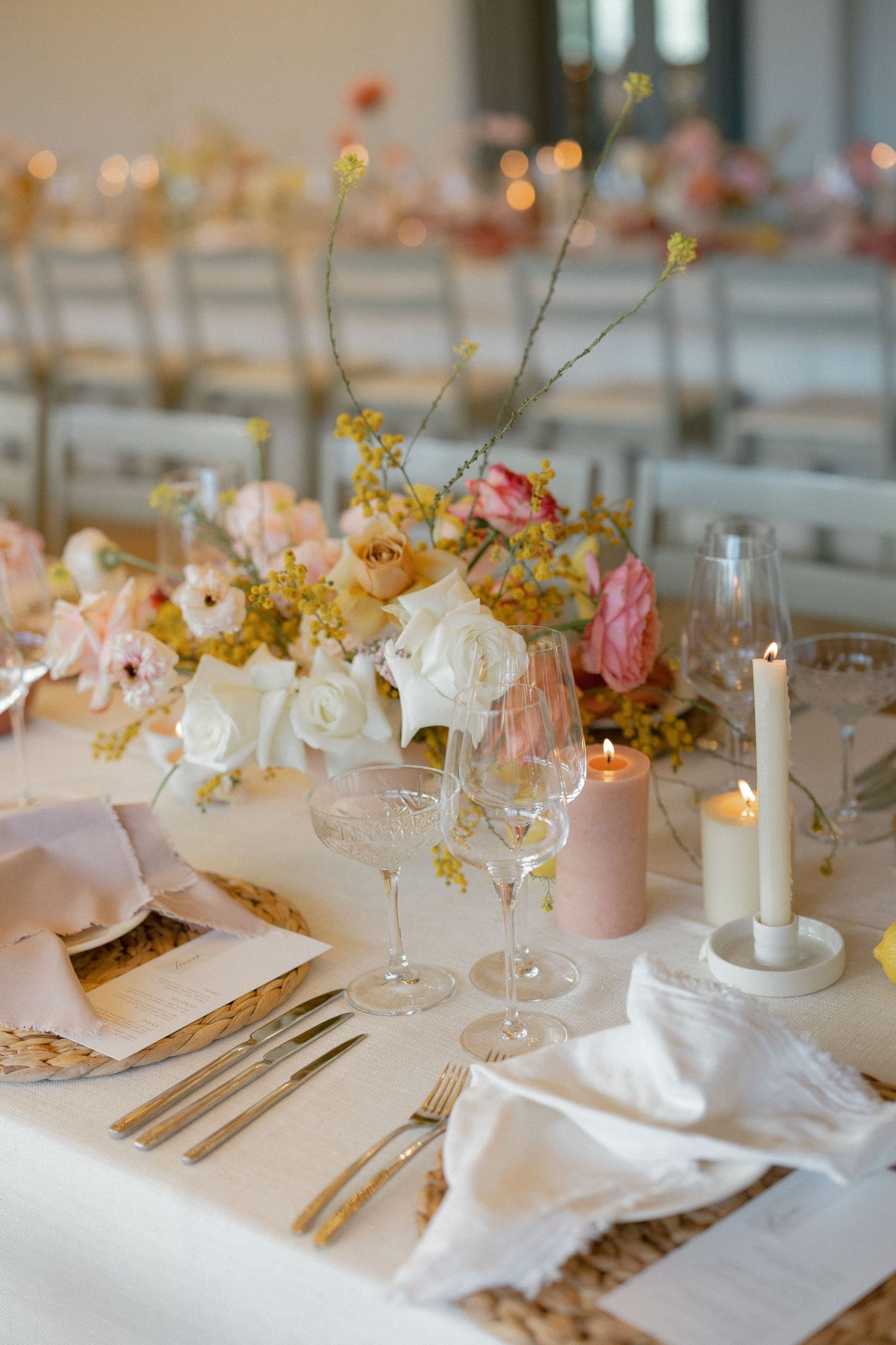 Romantic wedding tablescape with pink and white roses, crystal glassware, candles, and blush napkins.