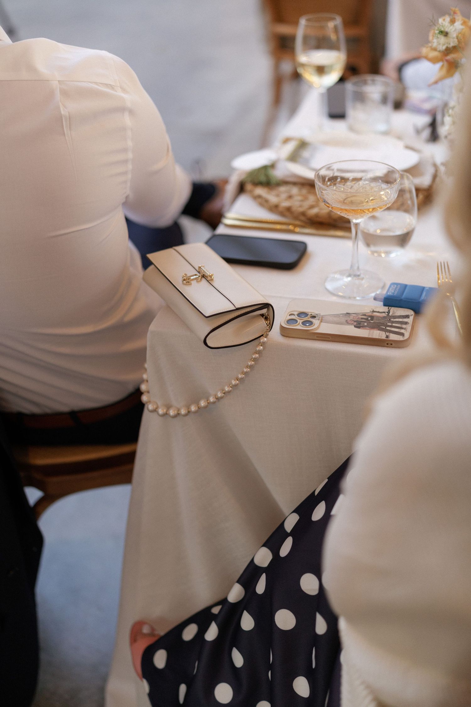 Elegant wedding reception table with pearl clutch purse, wine glasses, and white linen tablecloth.