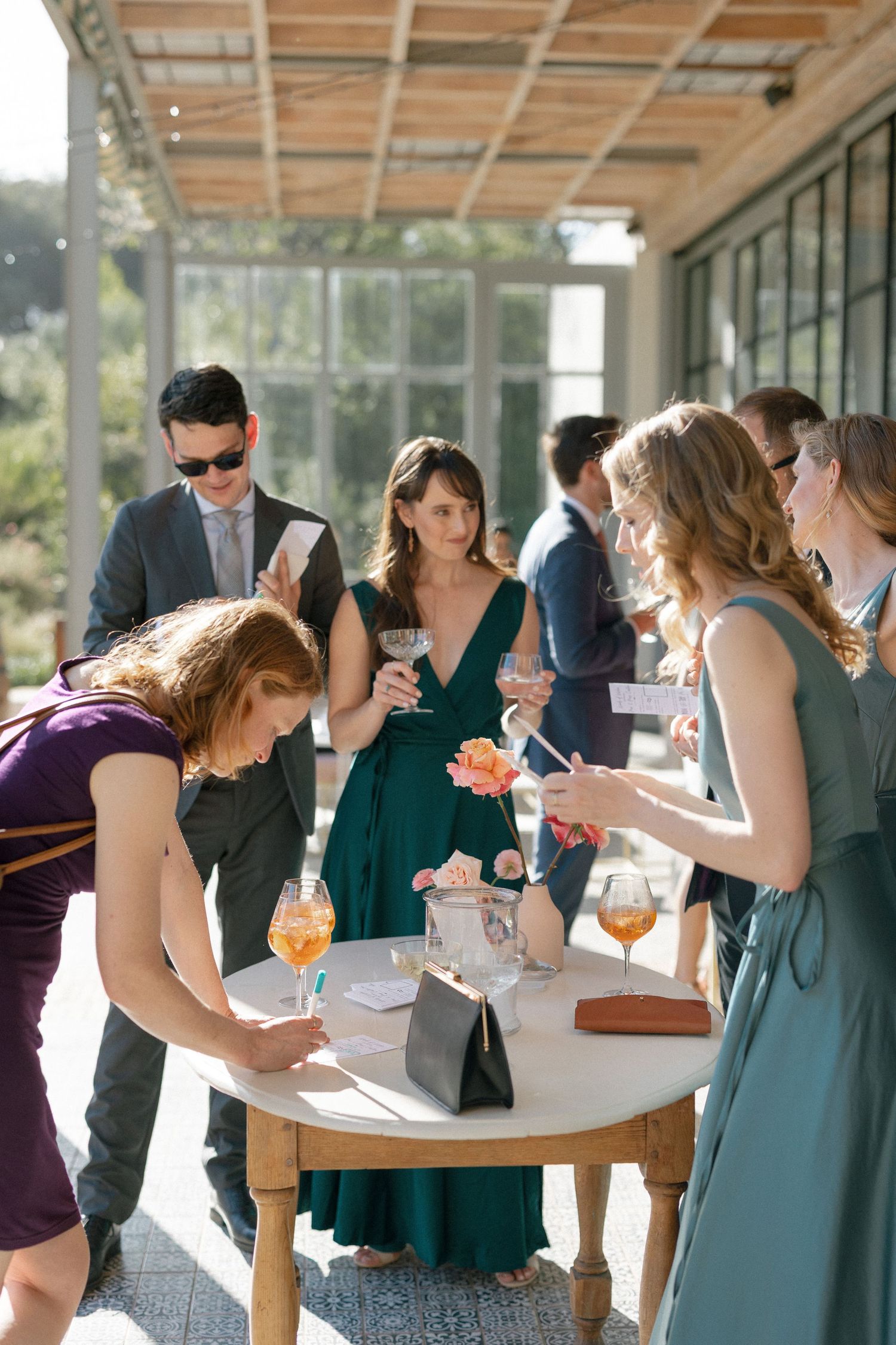 Wedding guests signing guestbook and socializing at outdoor cocktail hour reception tables.