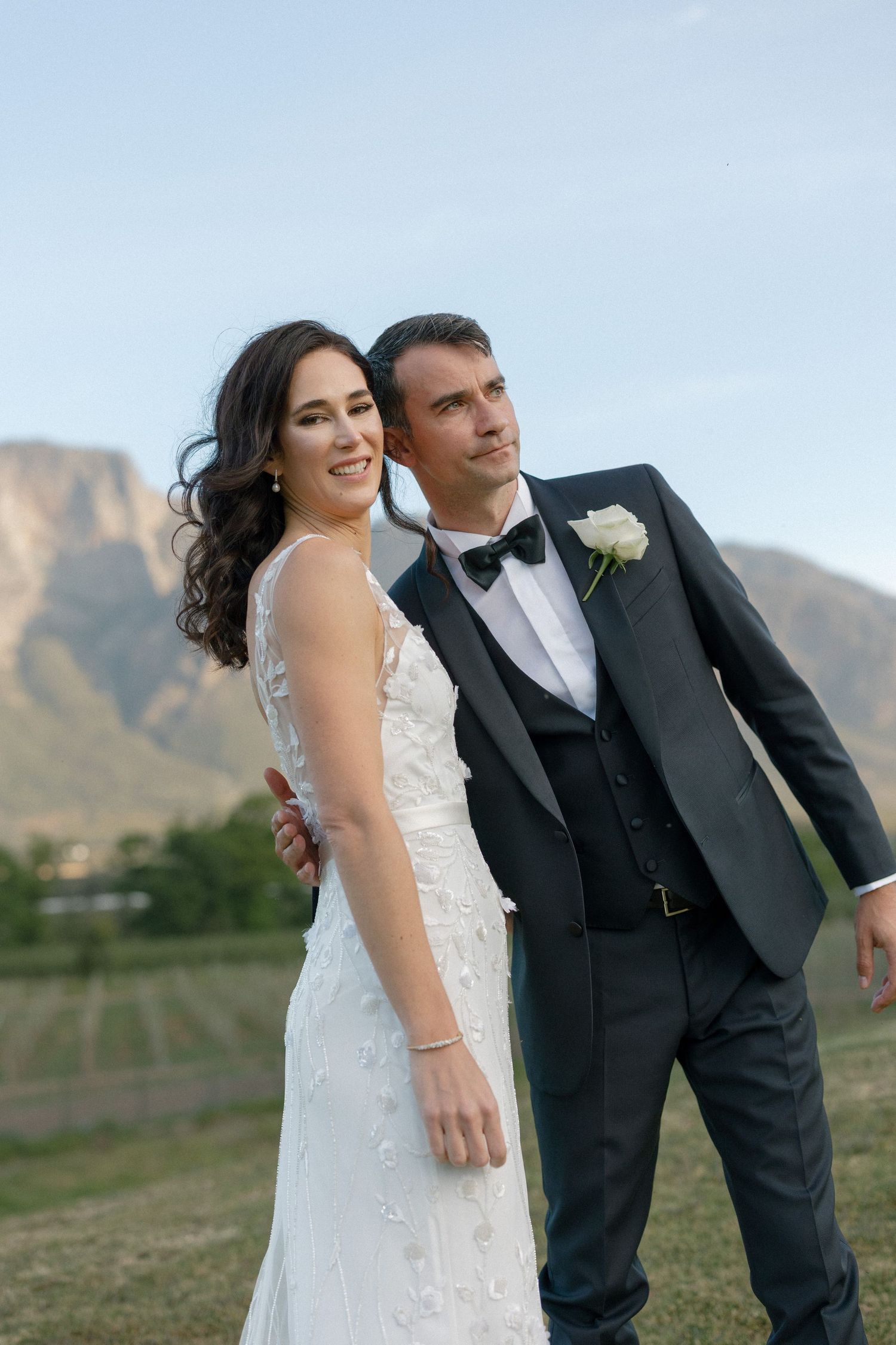 Bride and groom posing outdoors with mountain backdrop on their wedding day.