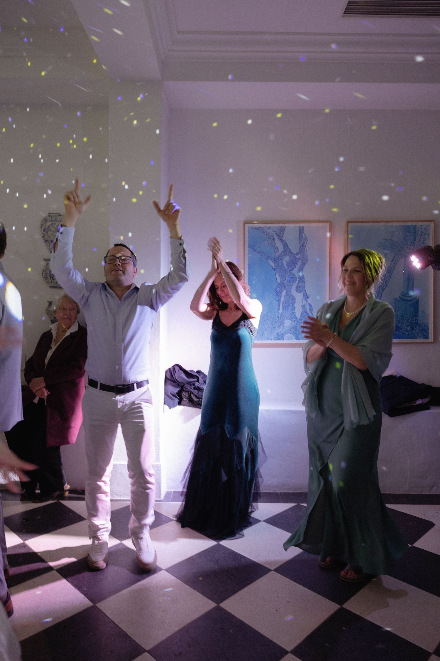 Guests dancing joyfully at an elegant party with confetti, checkered floor, and blue artwork on white walls.