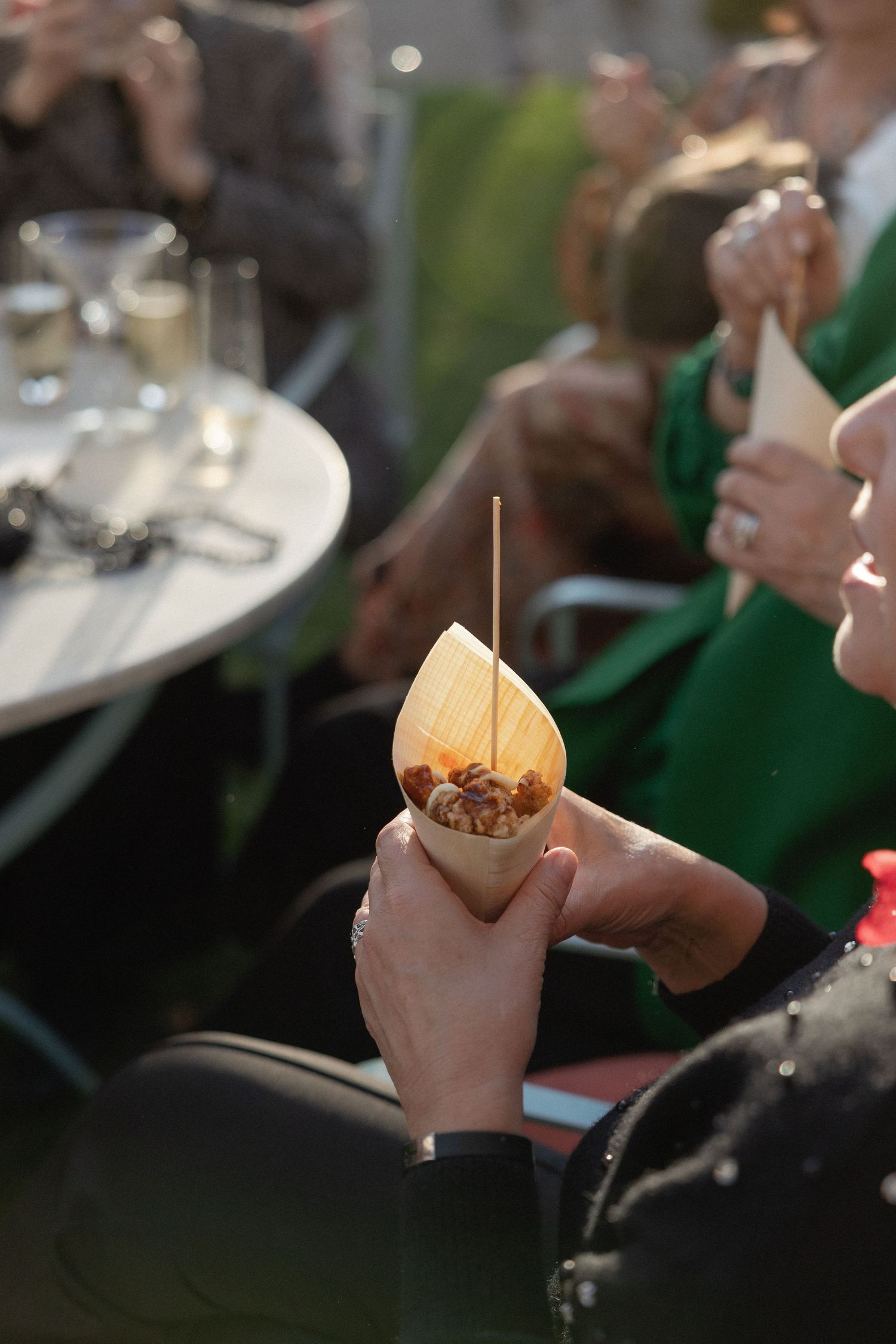 Hand holding a paper cone filled with appetizers at an outdoor wedding cocktail hour reception.