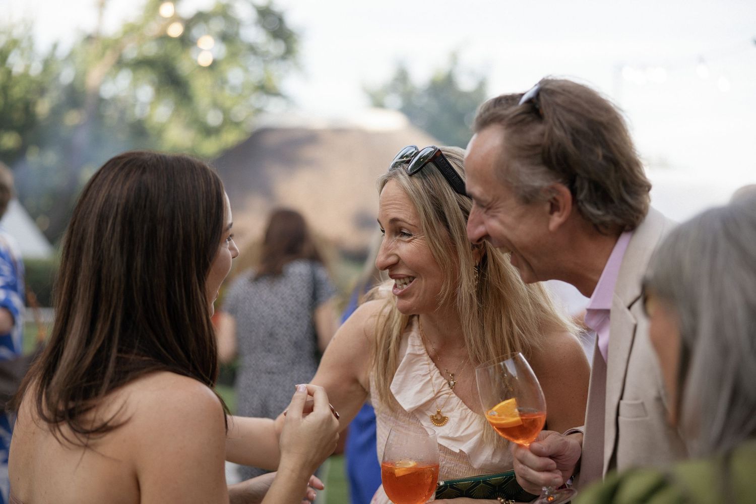 Three adults socializing outdoors at a garden party, smiling and holding cocktails.