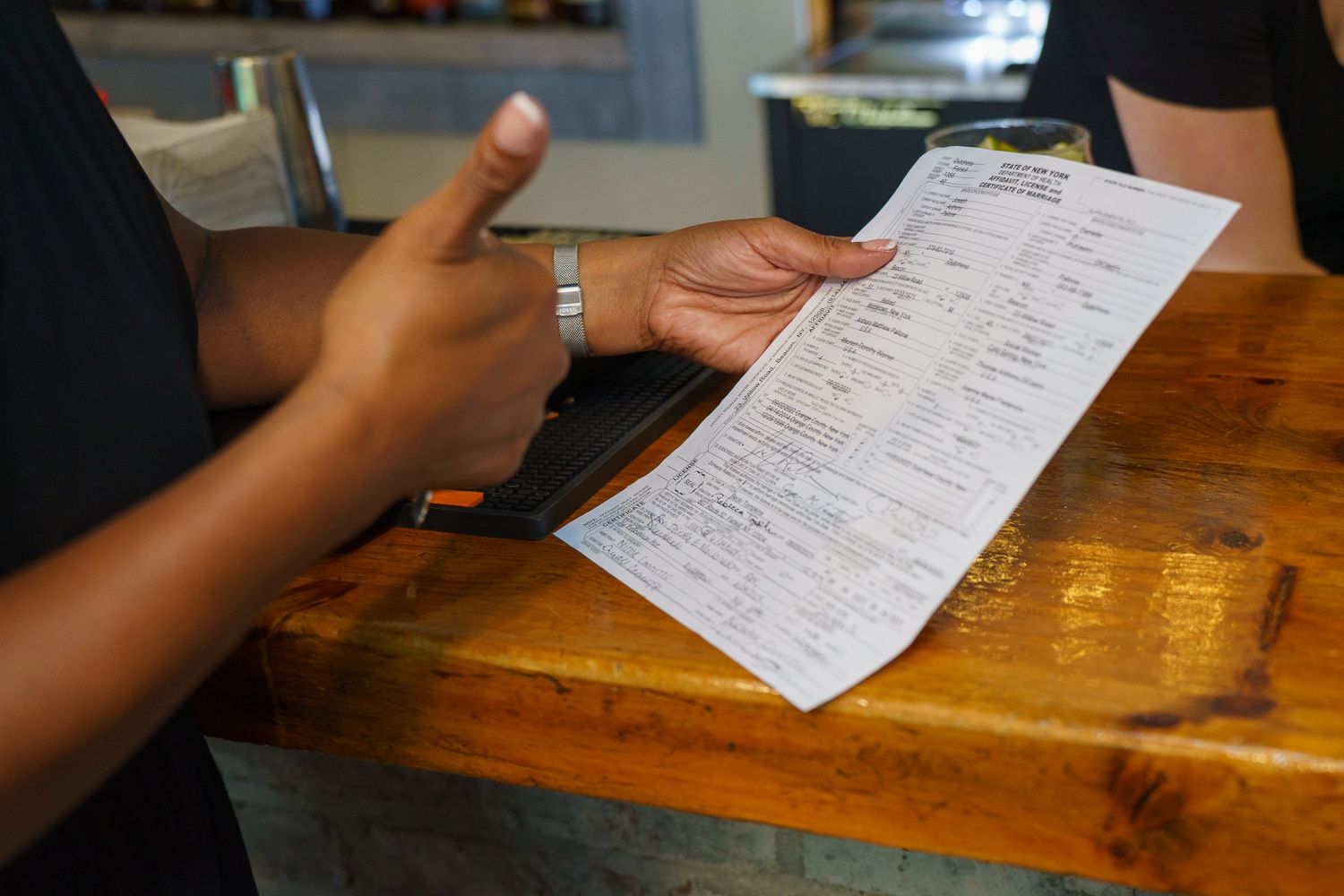 Person reviewing a restaurant menu at a wooden counter, holding a detailed paper menu in hand.