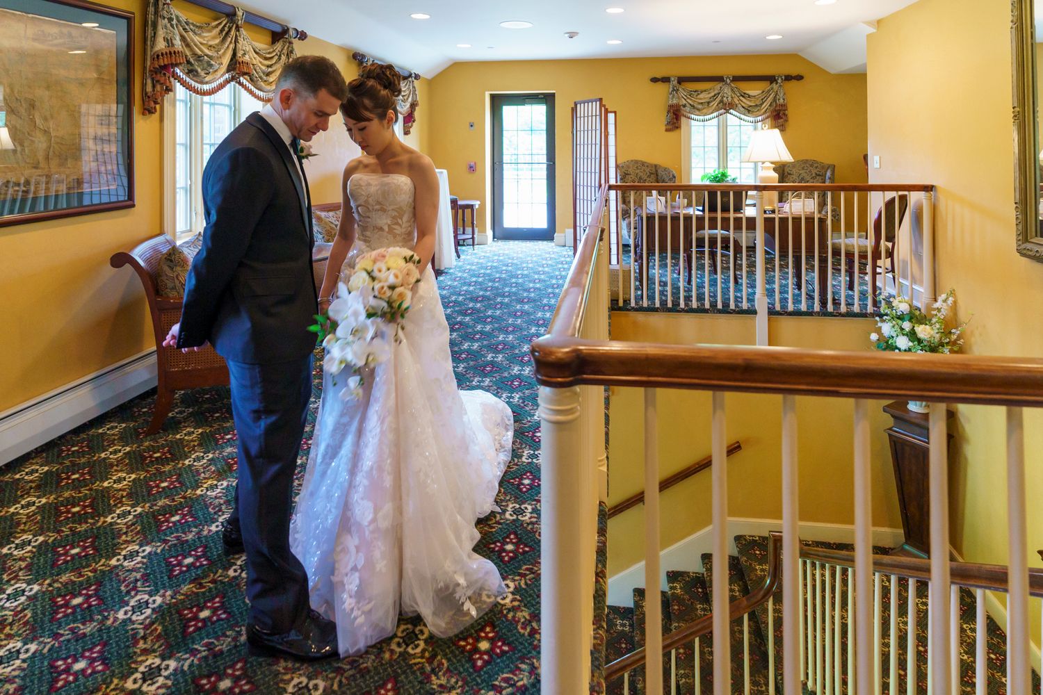Bride and groom share a tender moment on a staircase landing in an elegant venue with yellow walls.
