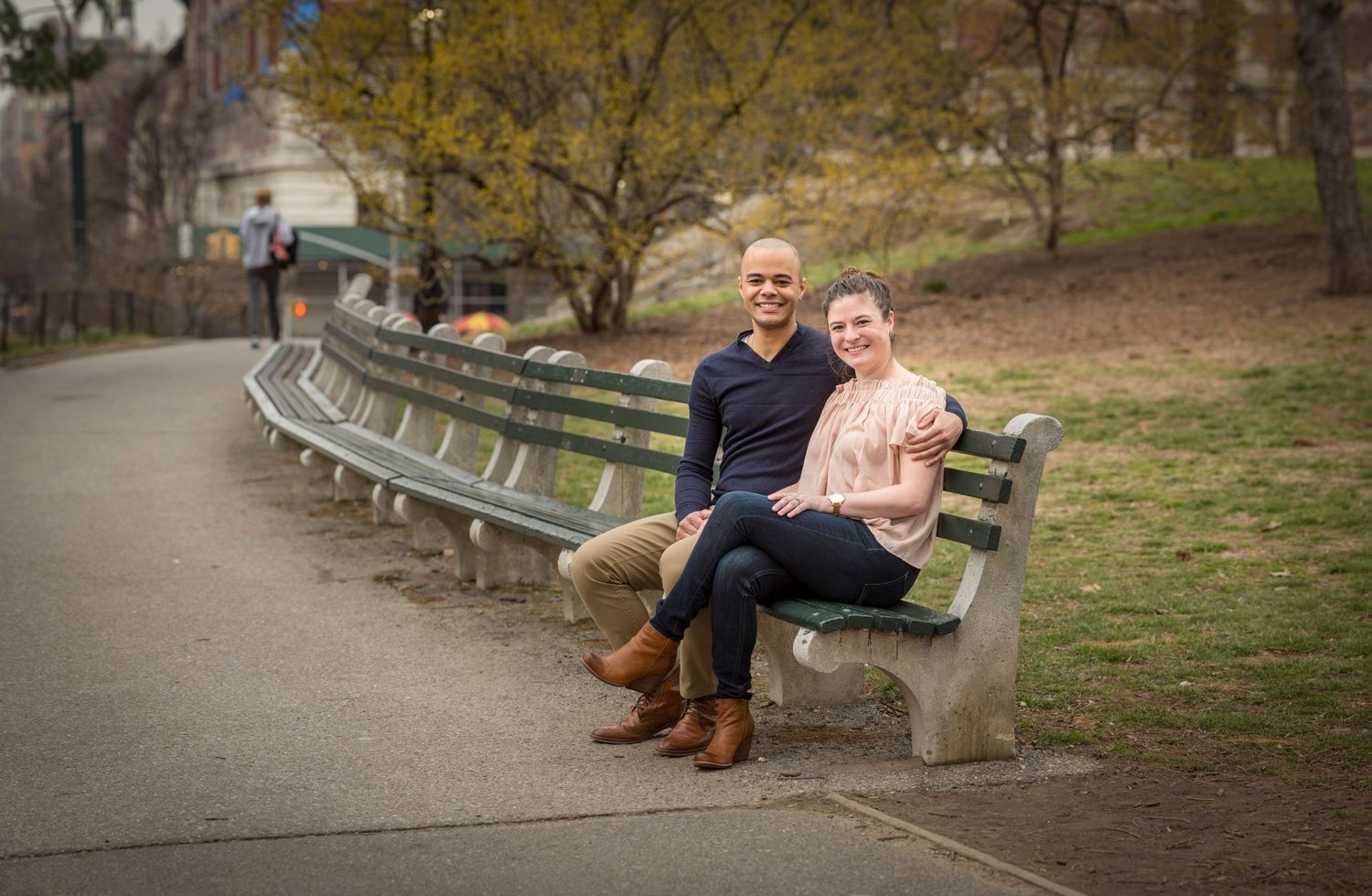 Couple sitting together on a park bench surrounded by autumn trees on a paved pathway.