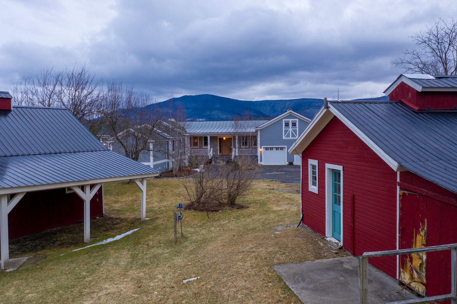 Red barn and farmhouse with mountain backdrop under cloudy skies in a rural New England setting.