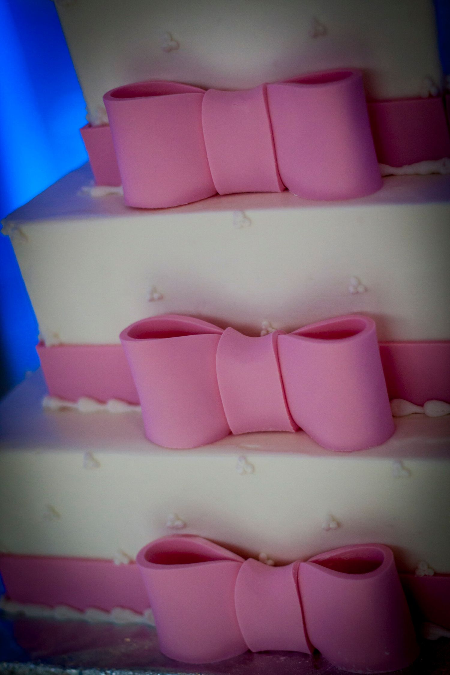 Three-tier white wedding cake decorated with pink fondant bows on each layer.