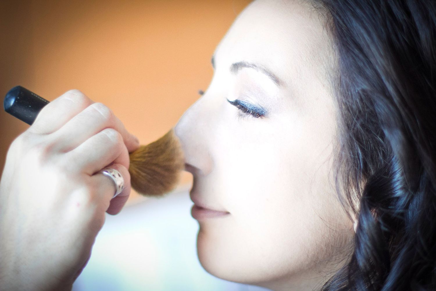 Bride receiving professional makeup application with powder brush before wedding ceremony.