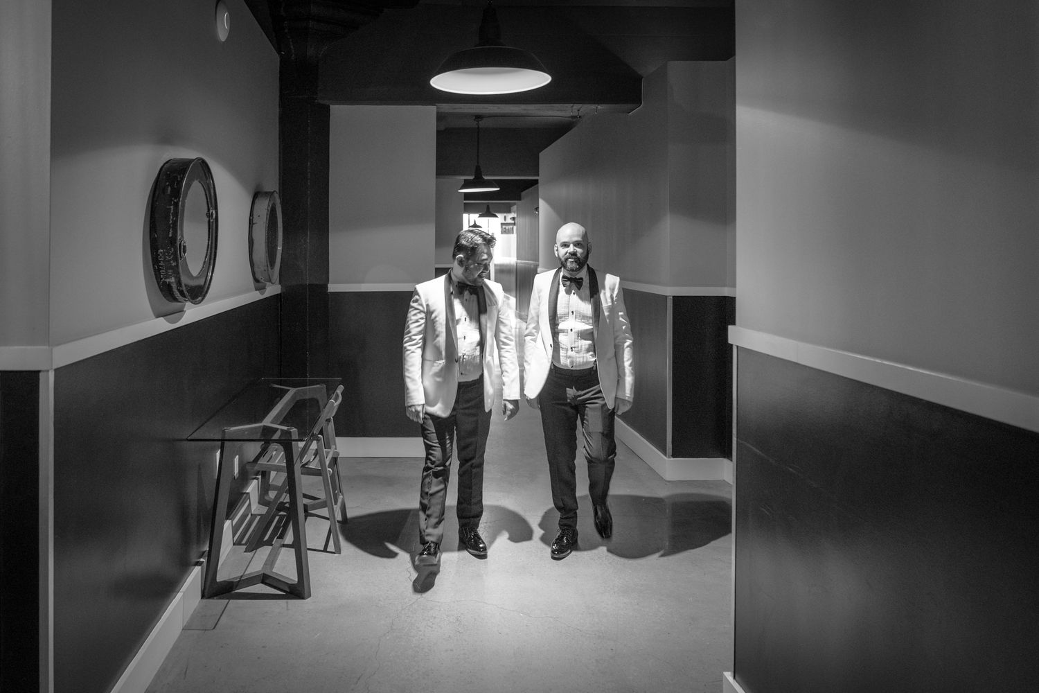Two men in white suits stand in a dimly lit hallway in a black and white photo.