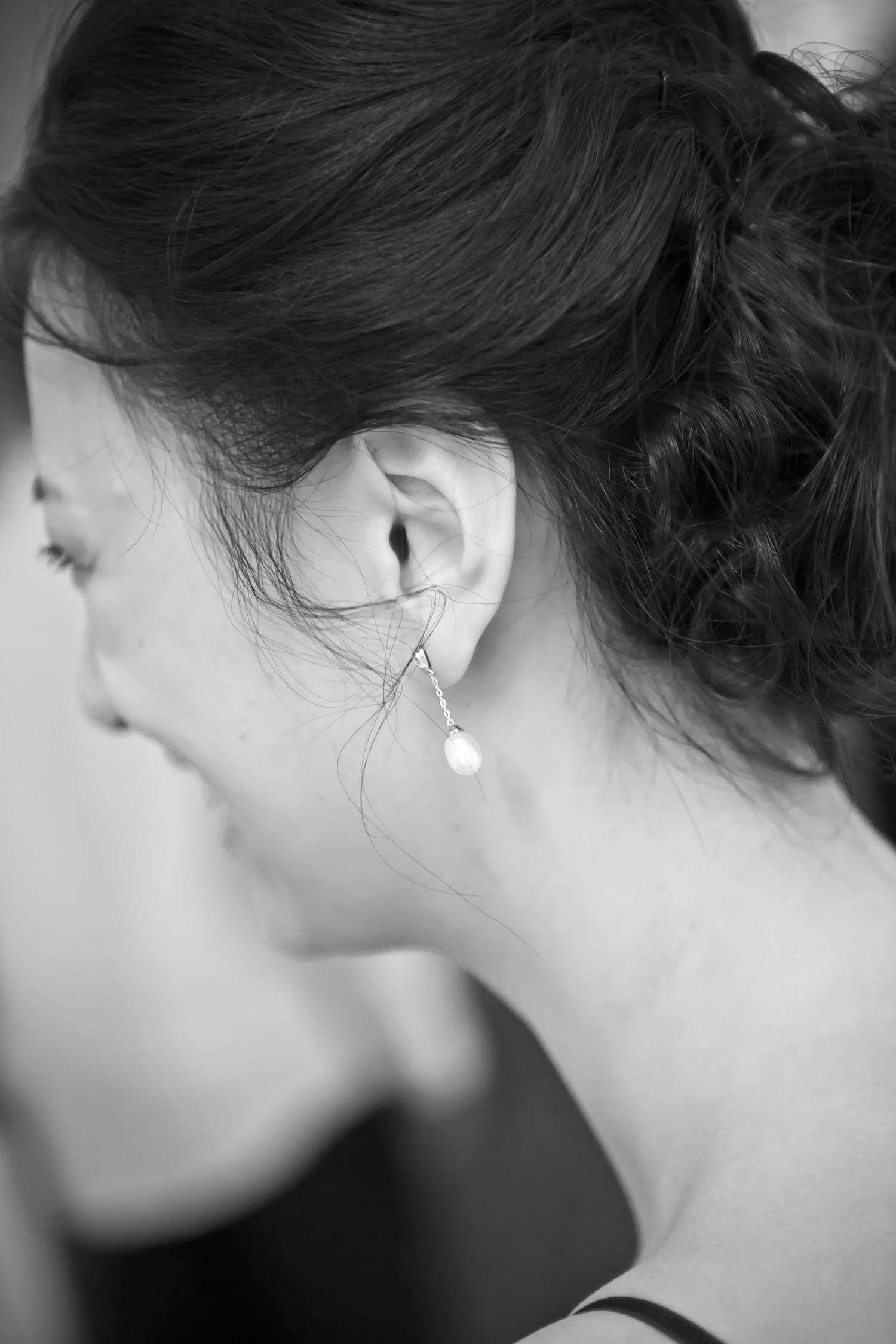 Black and white close-up of a womans elegant pearl drop earring with upswept hair.