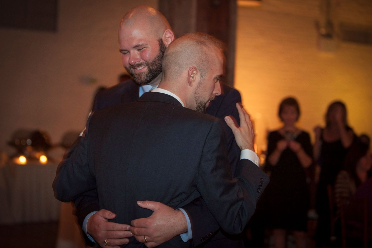 Two men in suits sharing an emotional embrace during first dance at wedding reception.