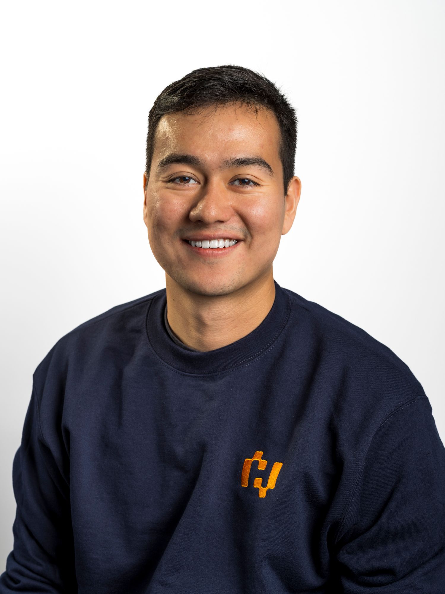 Smiling man in a navy blue sweatshirt with an orange logo against a white background.