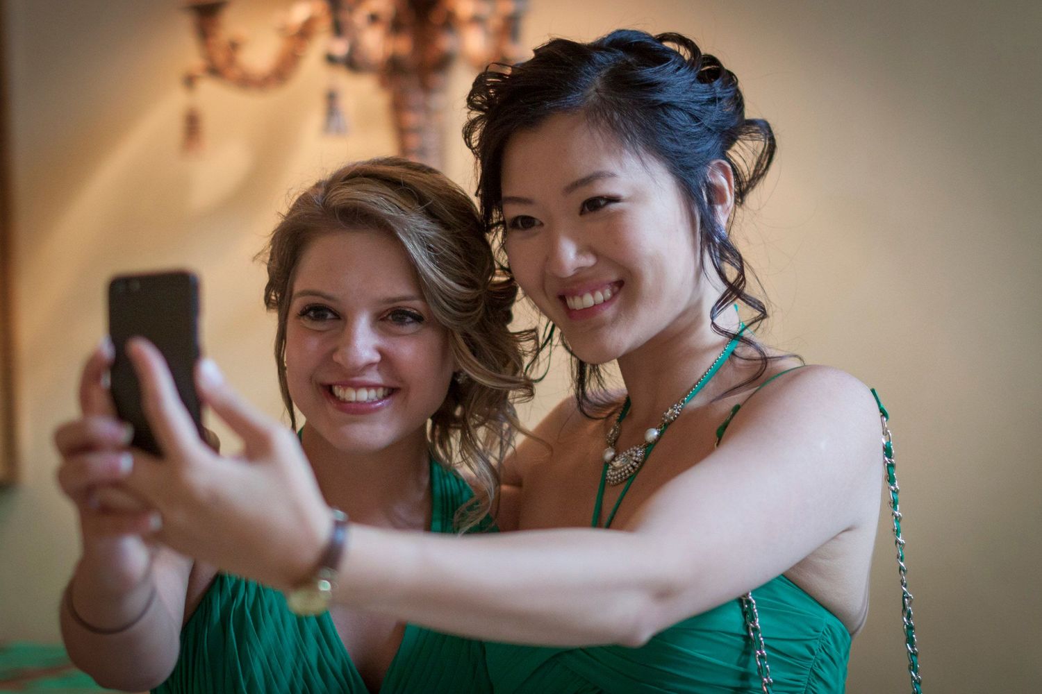 Two bridesmaids in green dresses taking a selfie together at a wedding celebration.