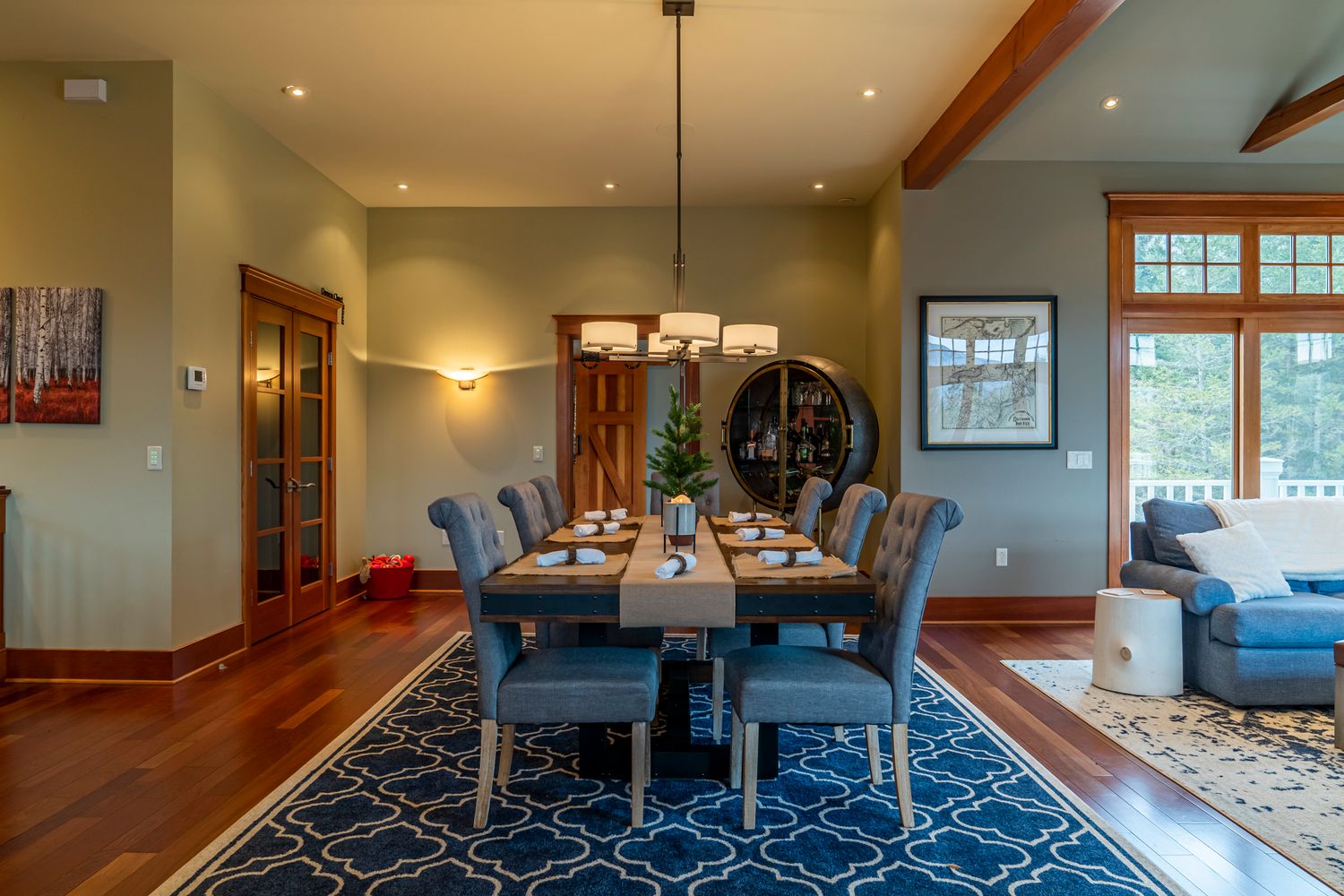 Elegant dining room with blue upholstered chairs, wooden table, chandelier, hardwood floors, and blue geometric area rug.
