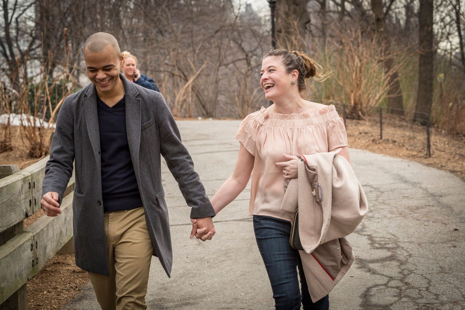 Happy couple holding hands and laughing while walking together on a park path in winter.