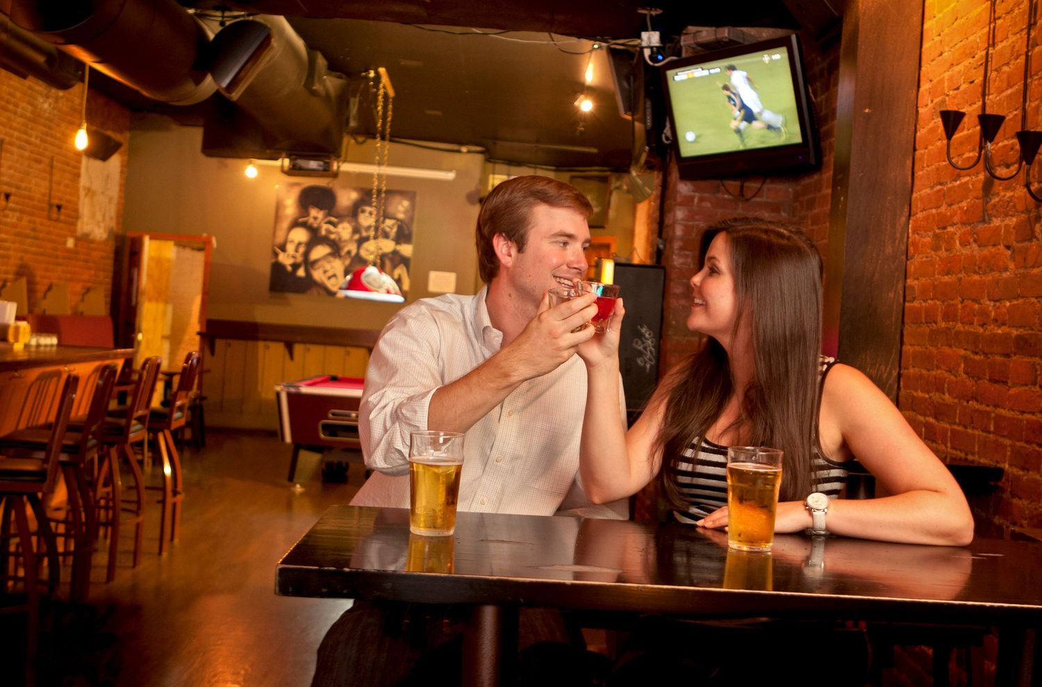 Man shows engagement ring to surprised woman while on a date at a casual bar restaurant.