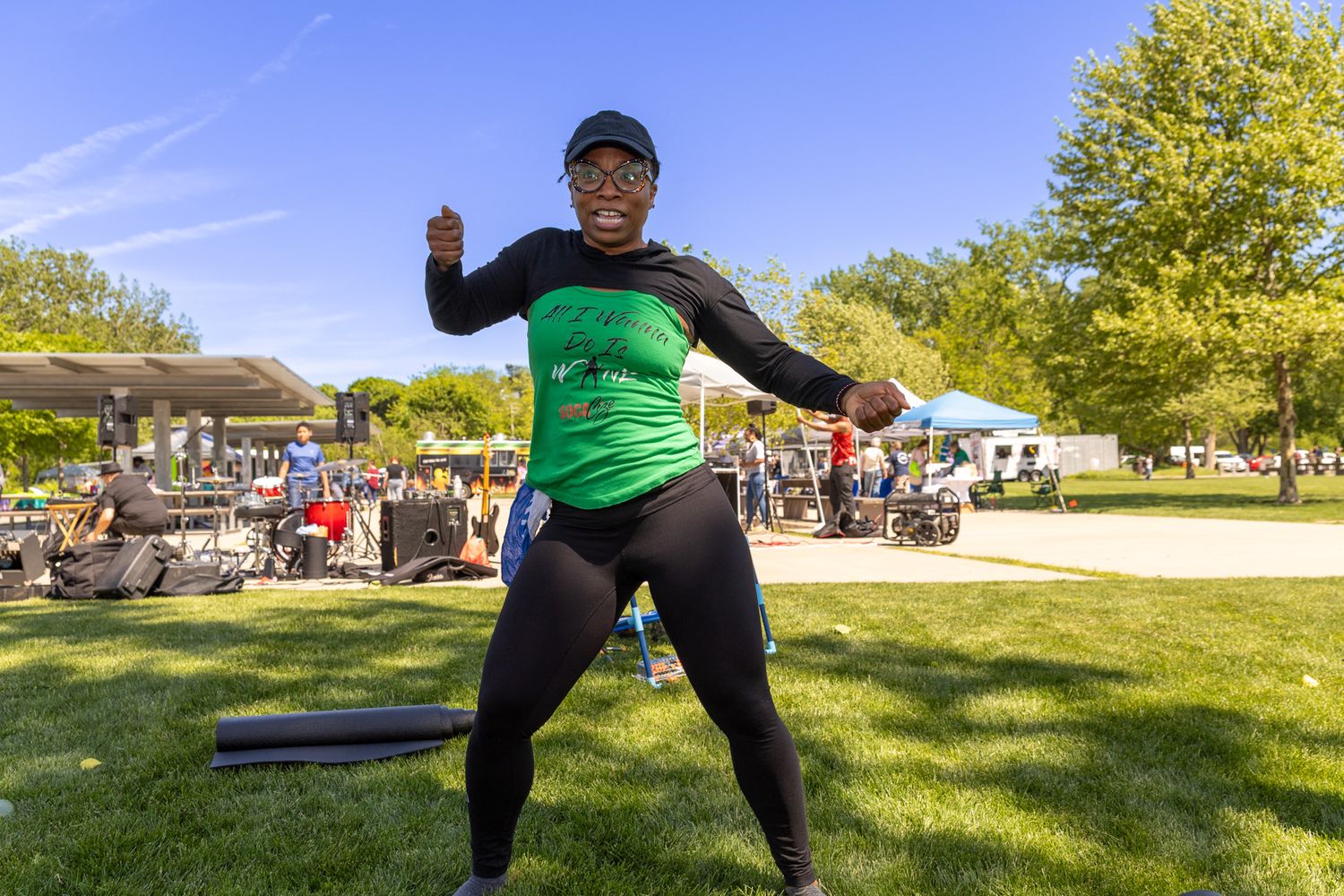 Energetic woman in green shirt and black cap dancing outdoors at a sunny park event.