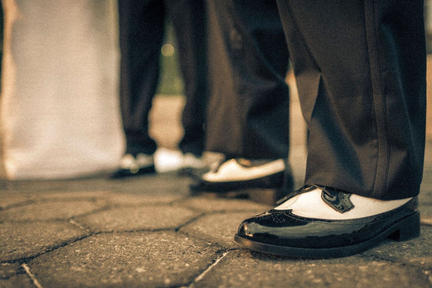 Groom wearing classic black and white two-tone dress shoes on cobblestone.