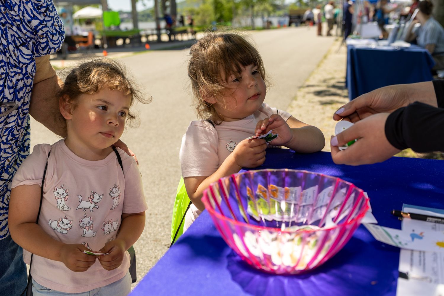 Two young girls at an outdoor event table examine items near a glowing pink decorative bowl.