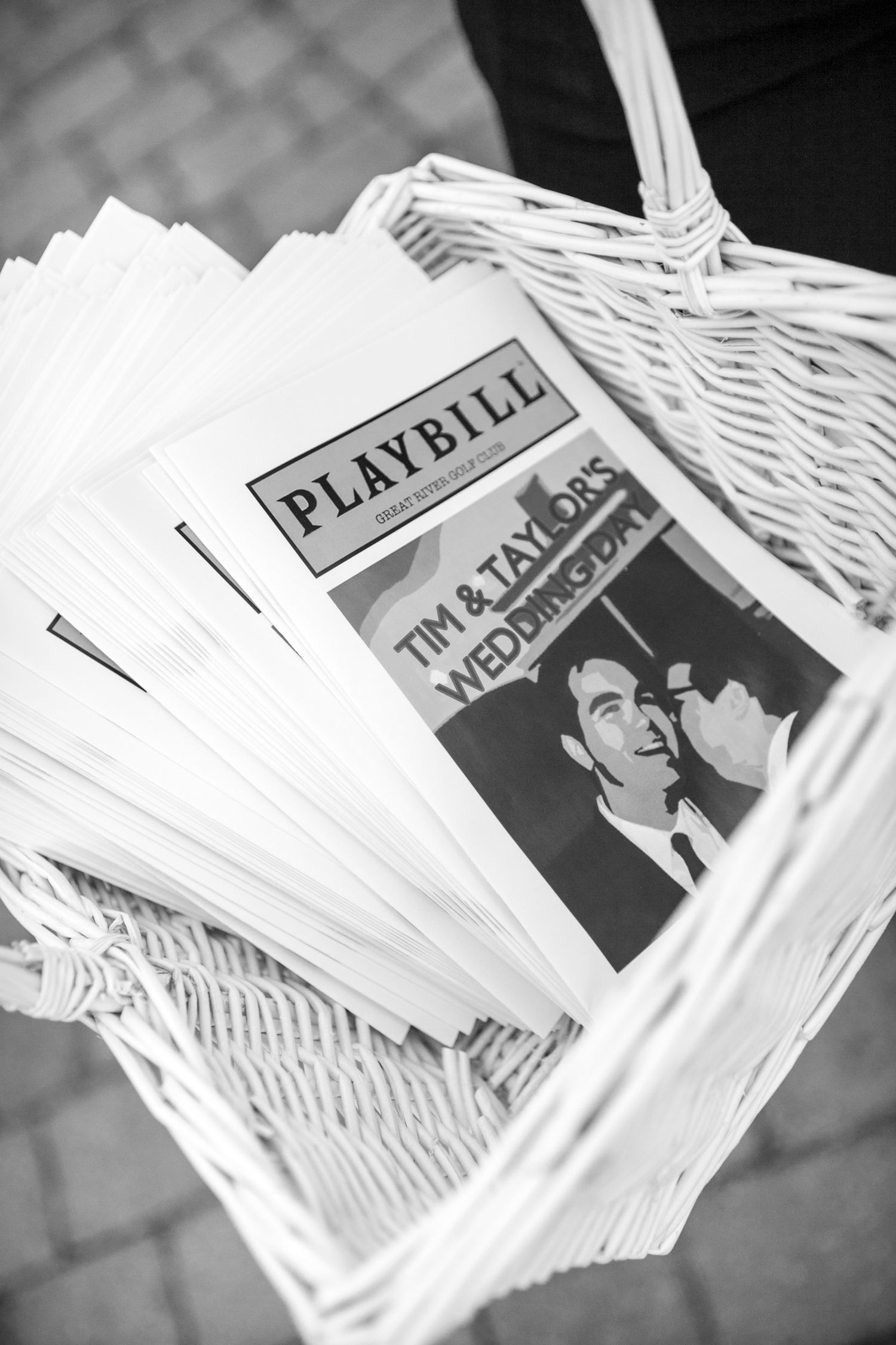 Black and white photo of Playbill wedding programs for Tim and Taylor's wedding day in a white wicker basket.