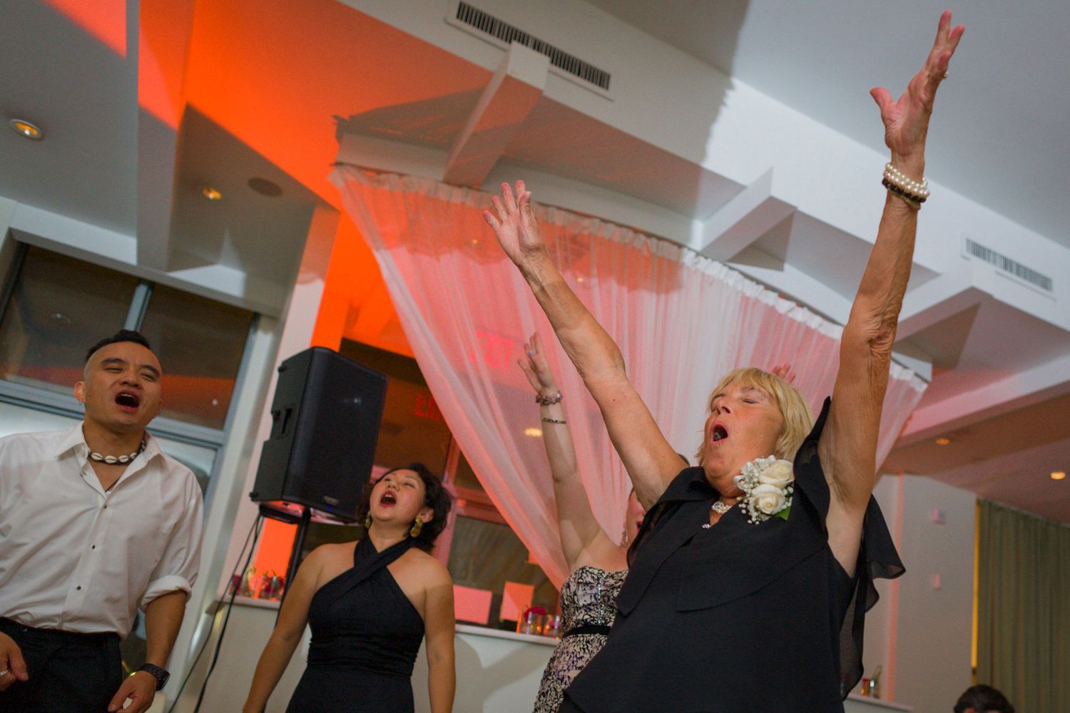 Wedding guests celebrating enthusiastically on dance floor with arms raised at reception.
