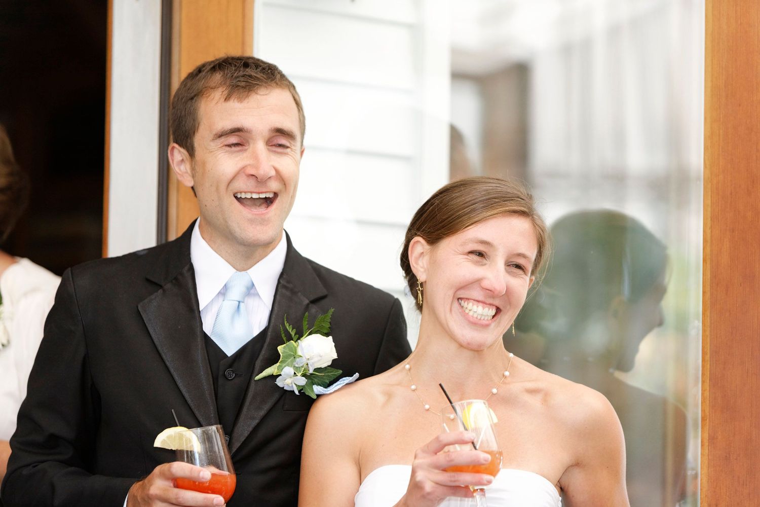 Smiling bride and groom holding cocktails at wedding reception celebration.