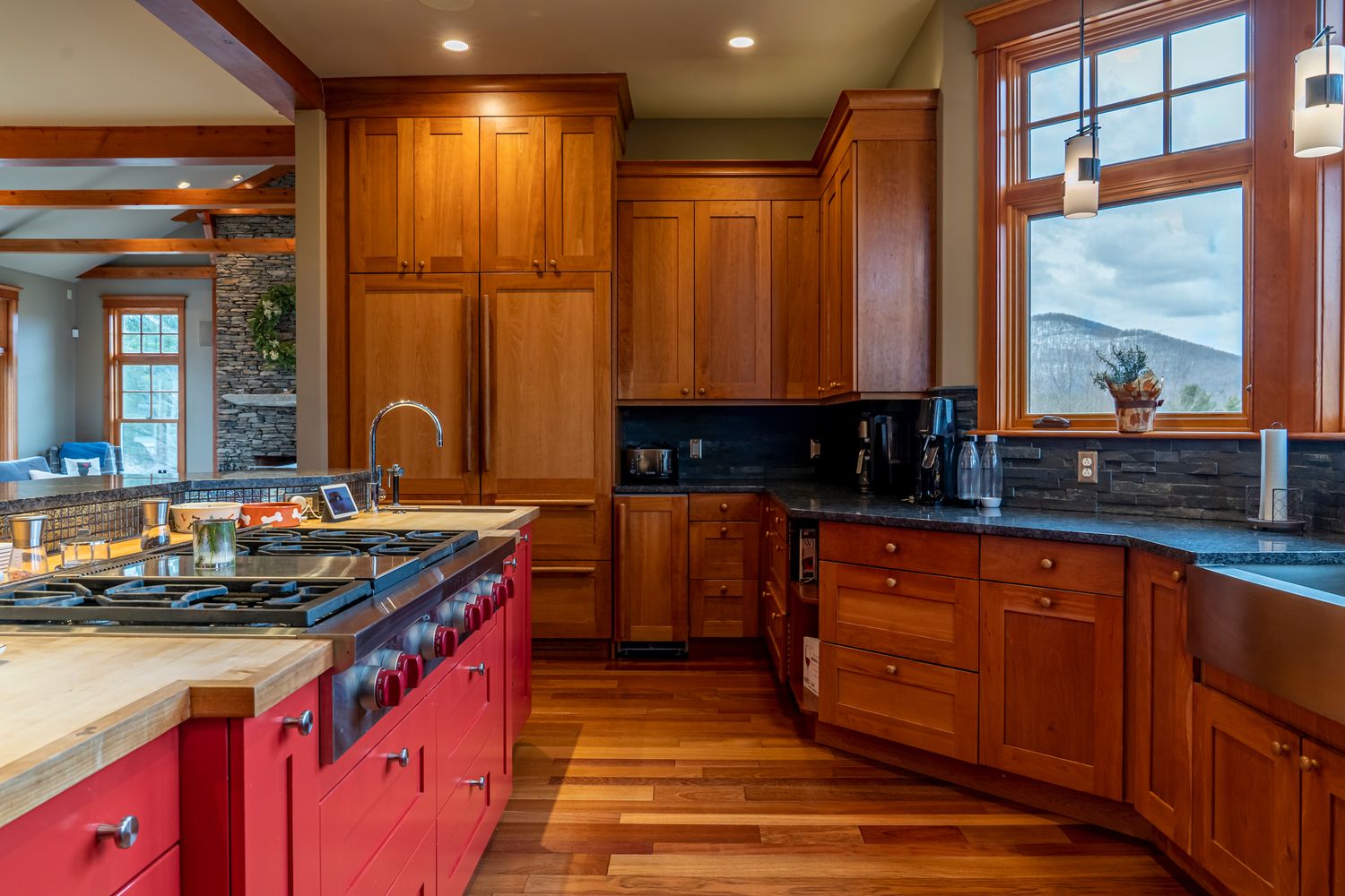Elegant kitchen with rich cherry wood cabinets, red island, hardwood floors, and mountain views.