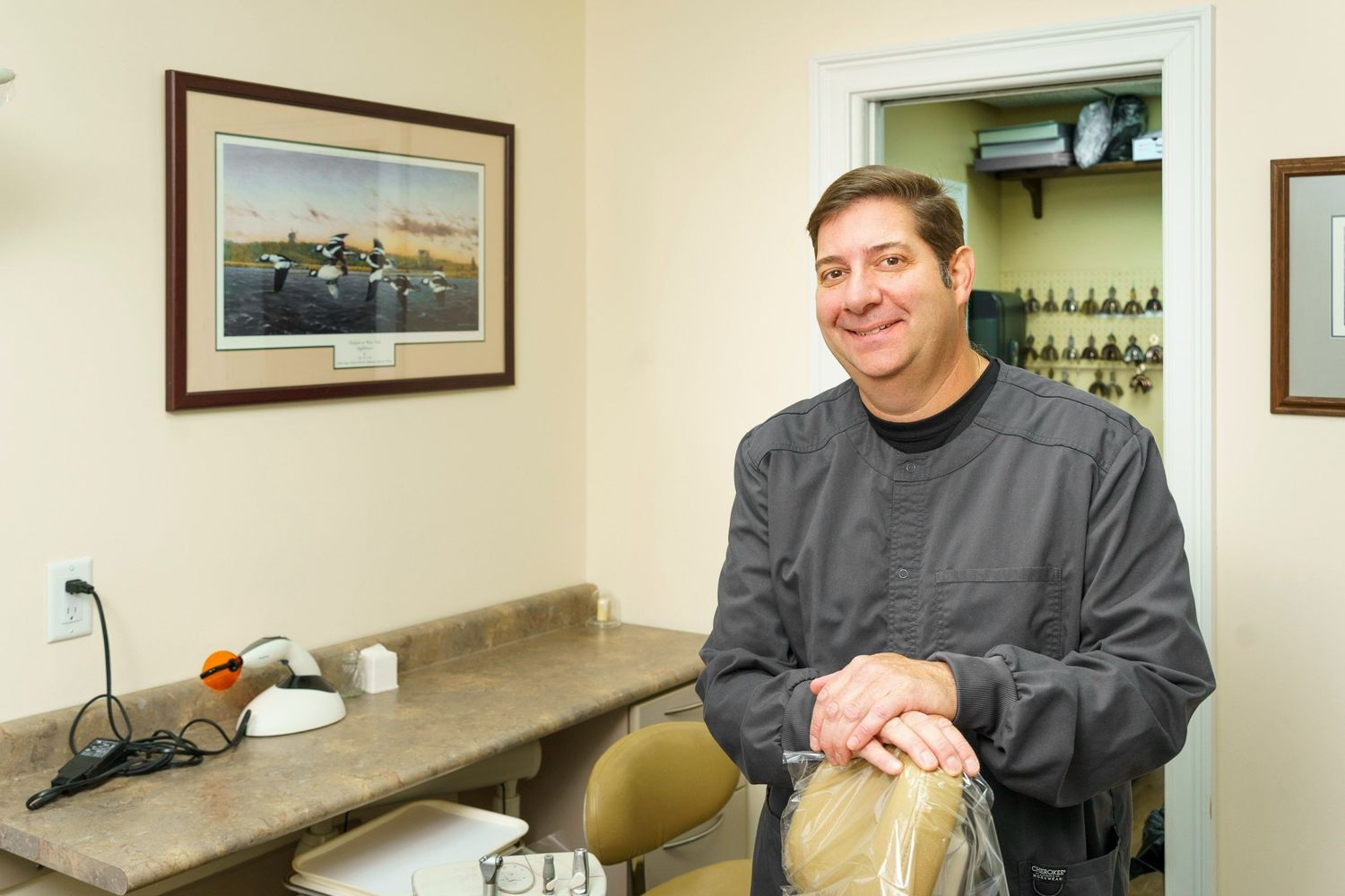 Smiling man in gray jacket standing in a medical office with framed artwork.