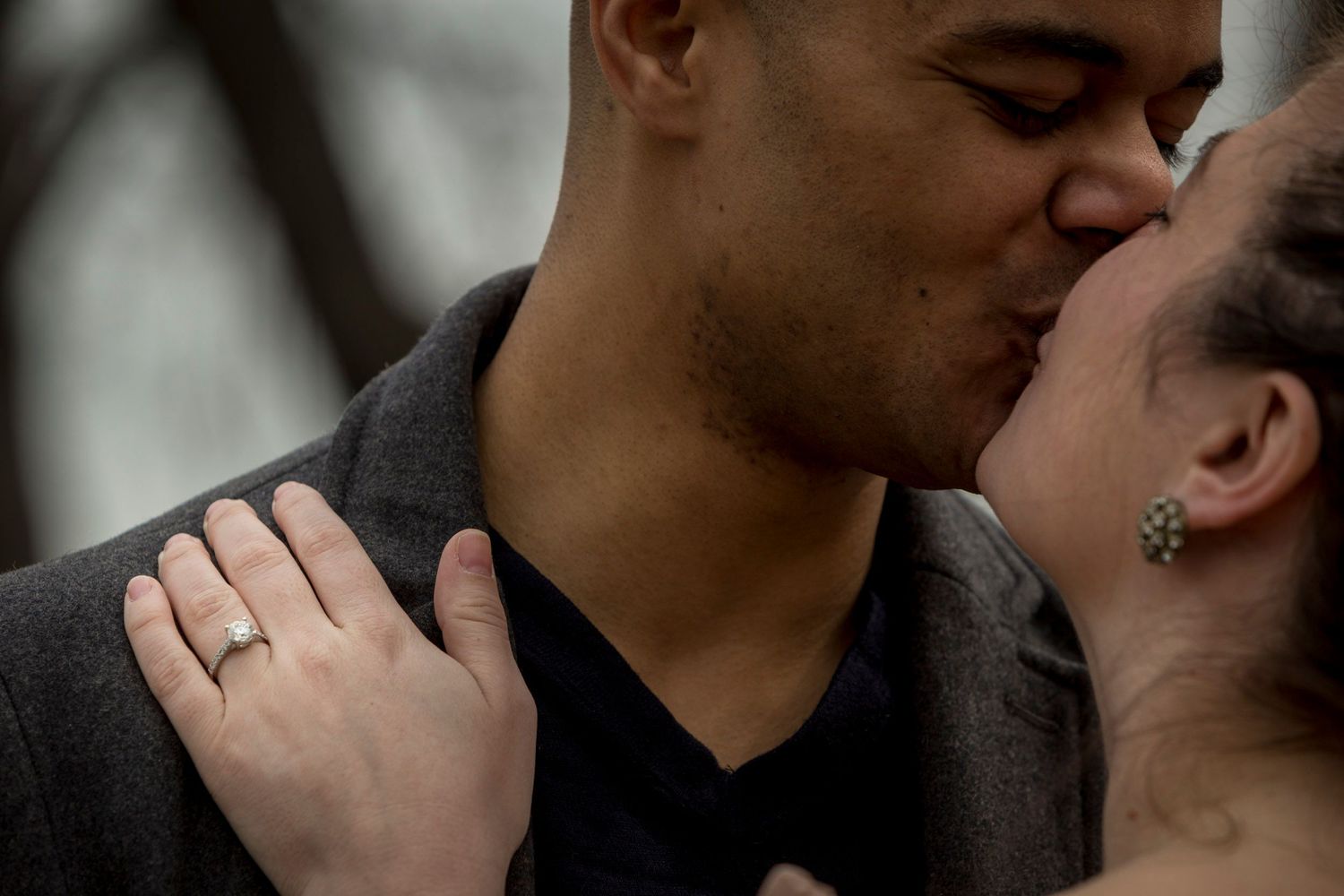 Close-up of couple sharing a kiss, engagement ring visible on woman's hand.