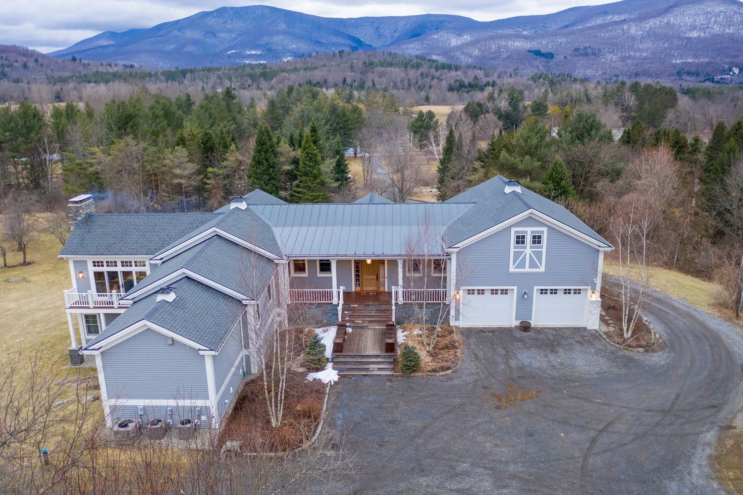 Aerial view of a large gray craftsman home with metal roof, surrounded by forests and mountain views.