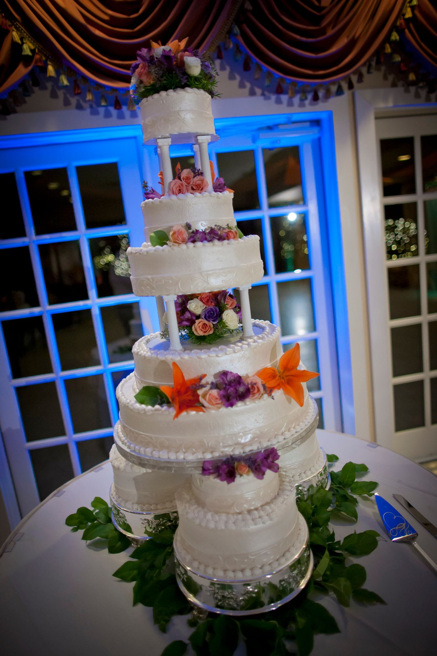 Elegant five-tier white wedding cake decorated with colorful flowers on display at reception.