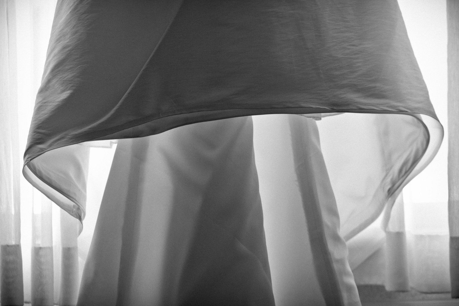 Artistic black and white shot of flowing wedding dress hanging near bright window.
