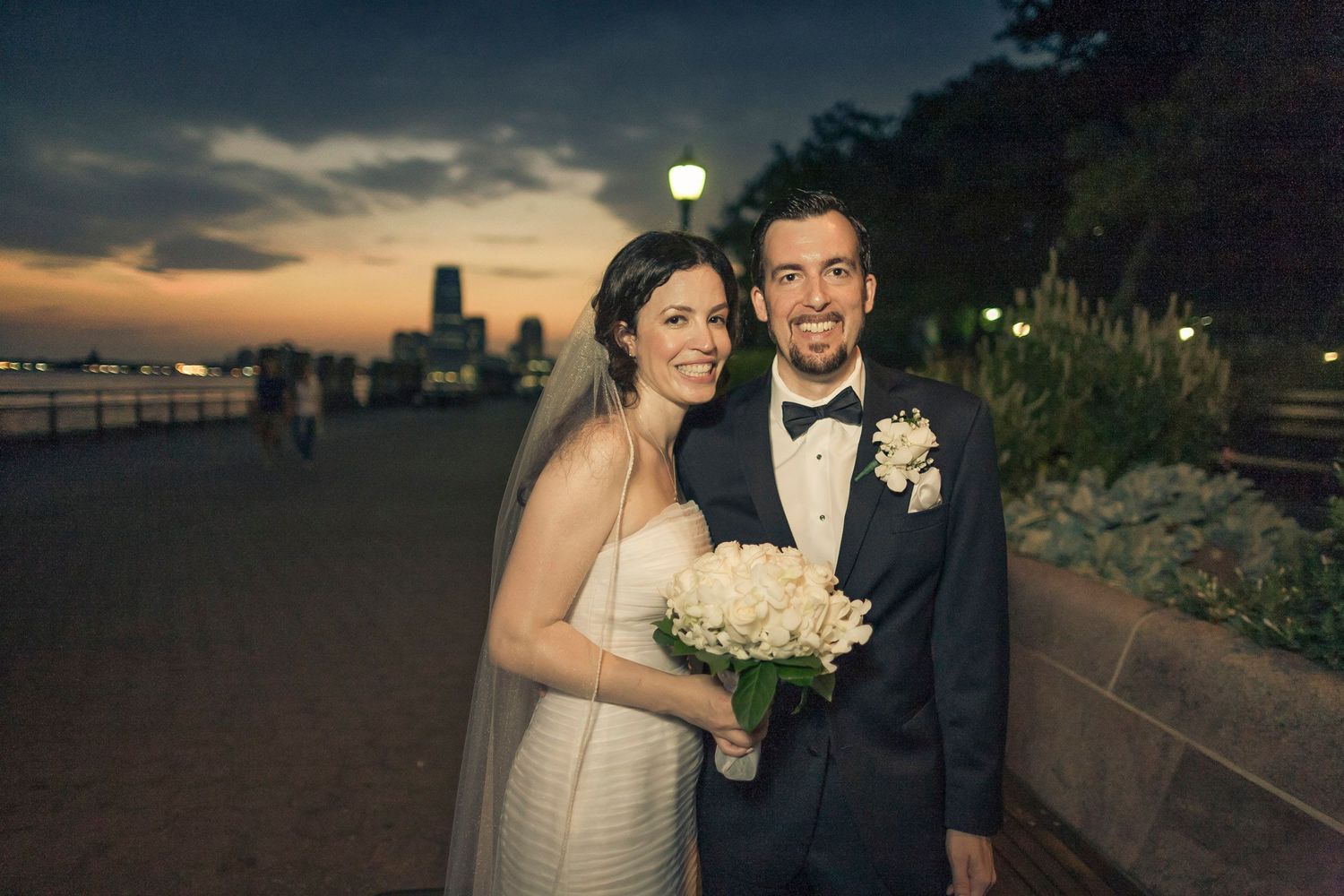 Bride and groom pose together at sunset with city skyline in the background.