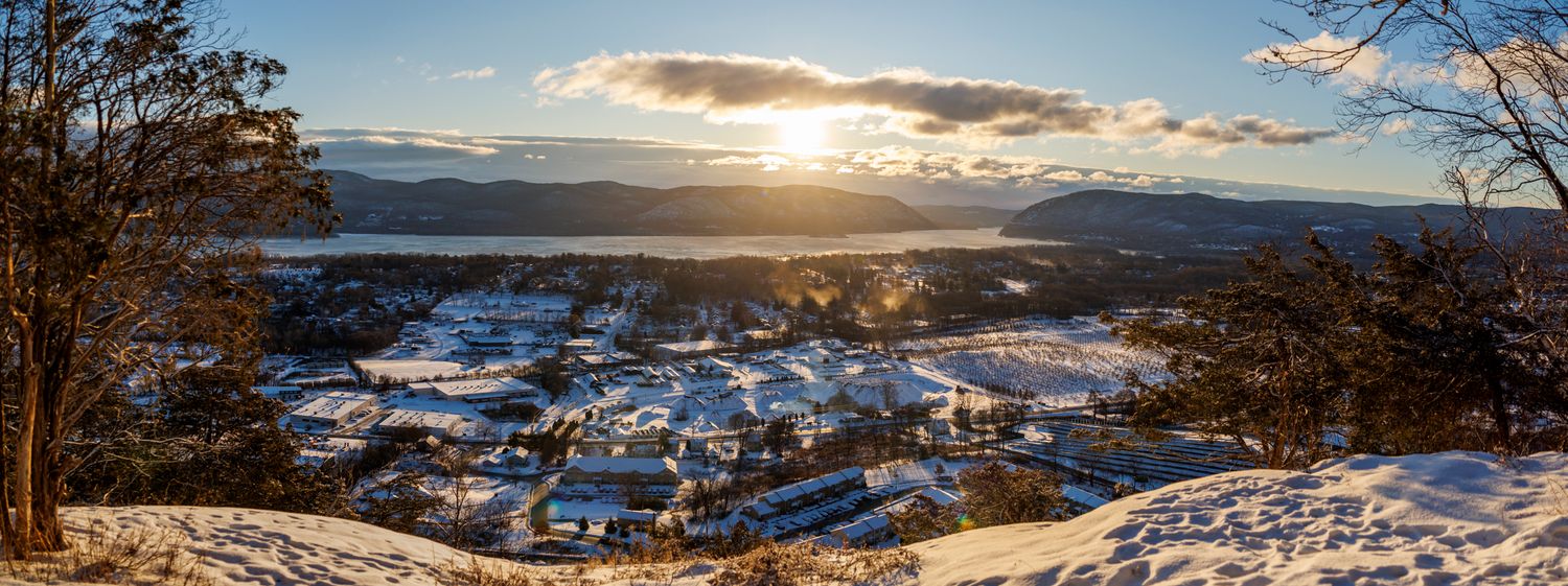 Panoramic winter sunset view over a snow-covered town with mountains and dramatic clouds in the background.