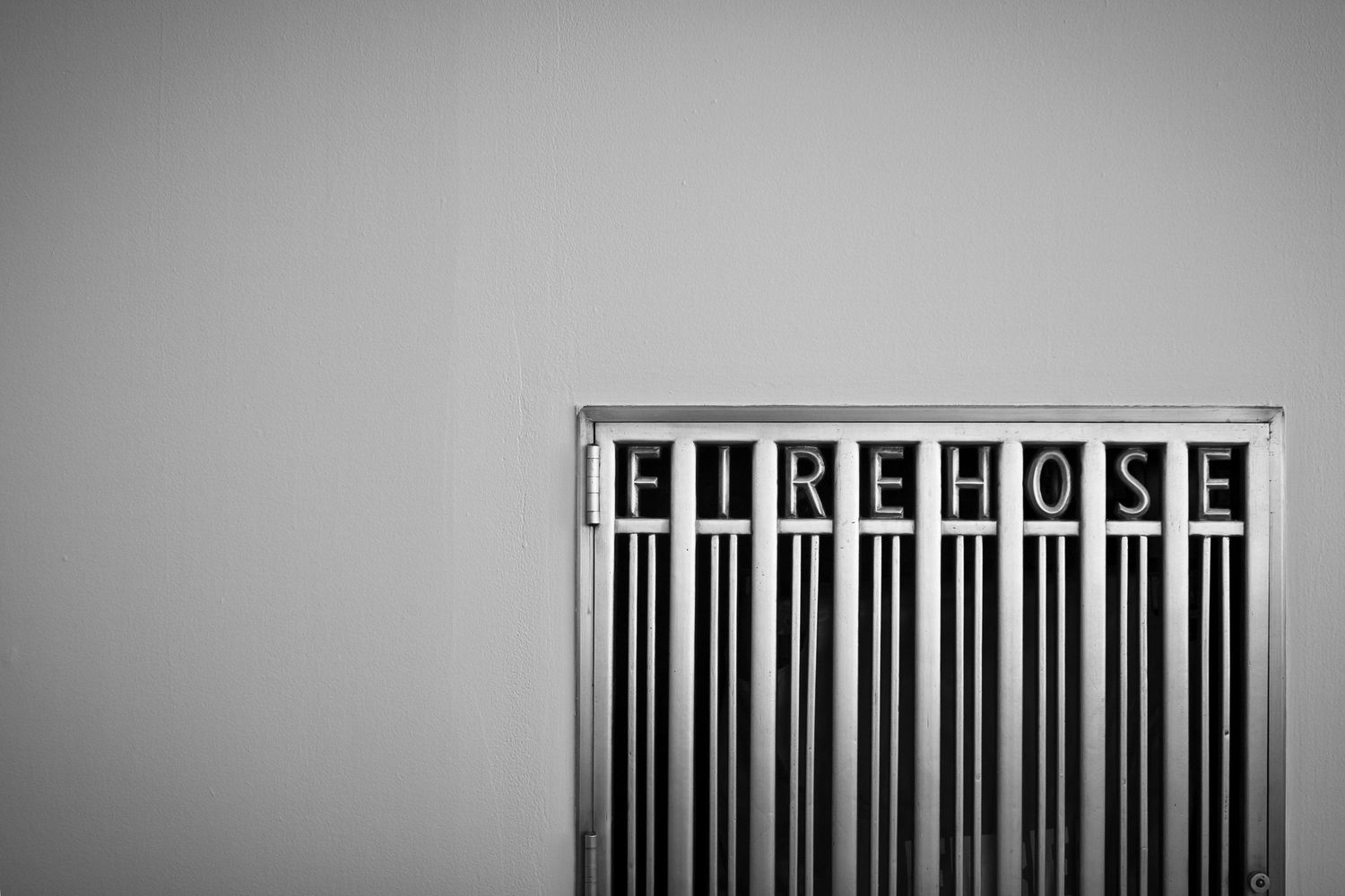 Black and white photo of a metal fire hose cabinet mounted on a gray wall.