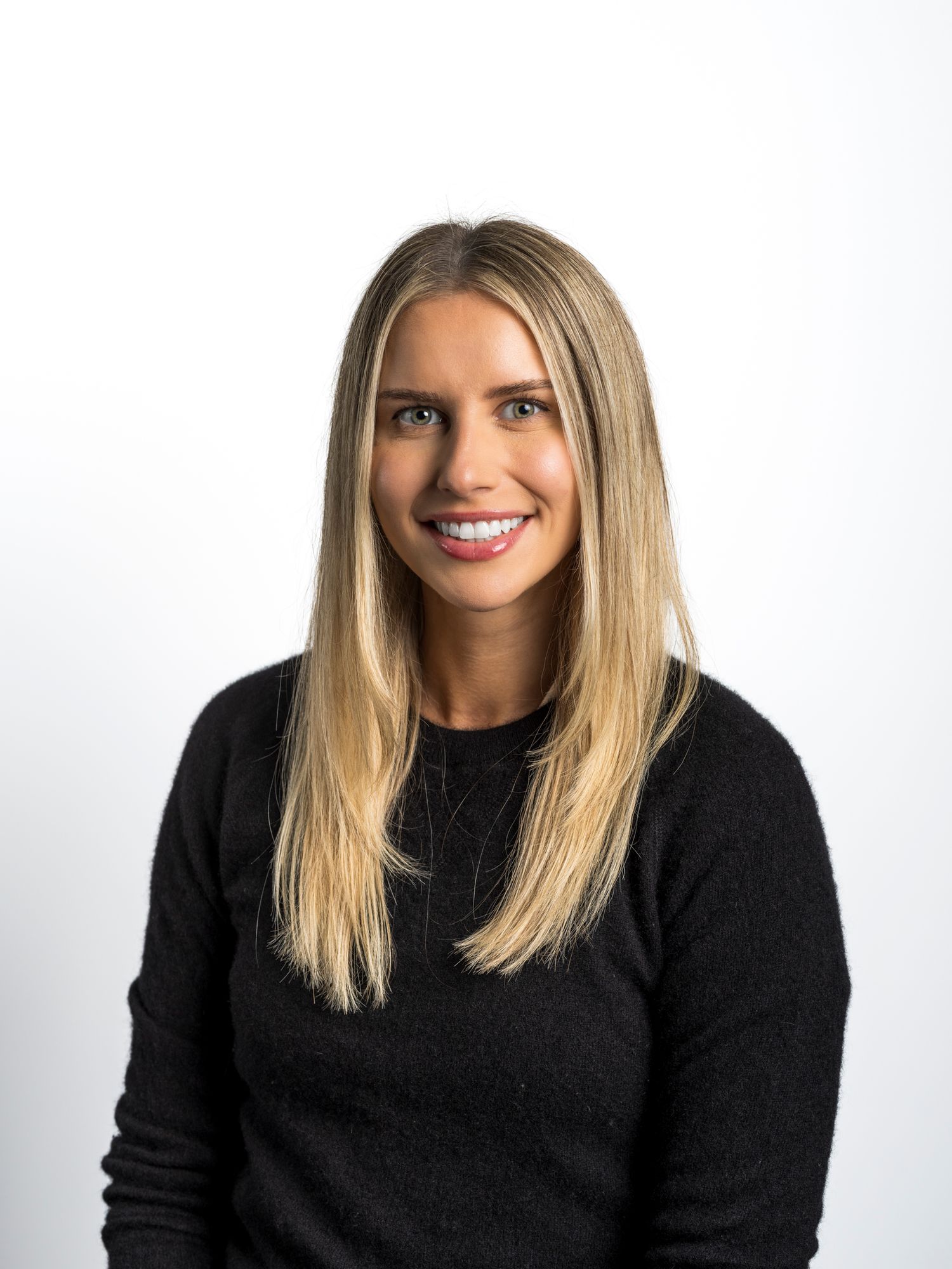 Smiling blonde woman in black sweater poses for professional headshot against white background.
