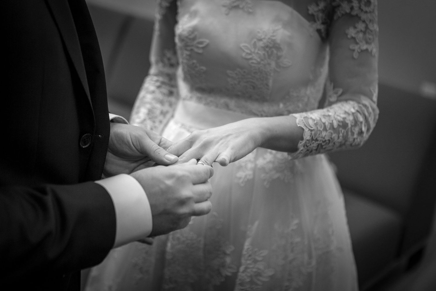 Black and white photo of bride and groom exchanging rings during wedding ceremony.