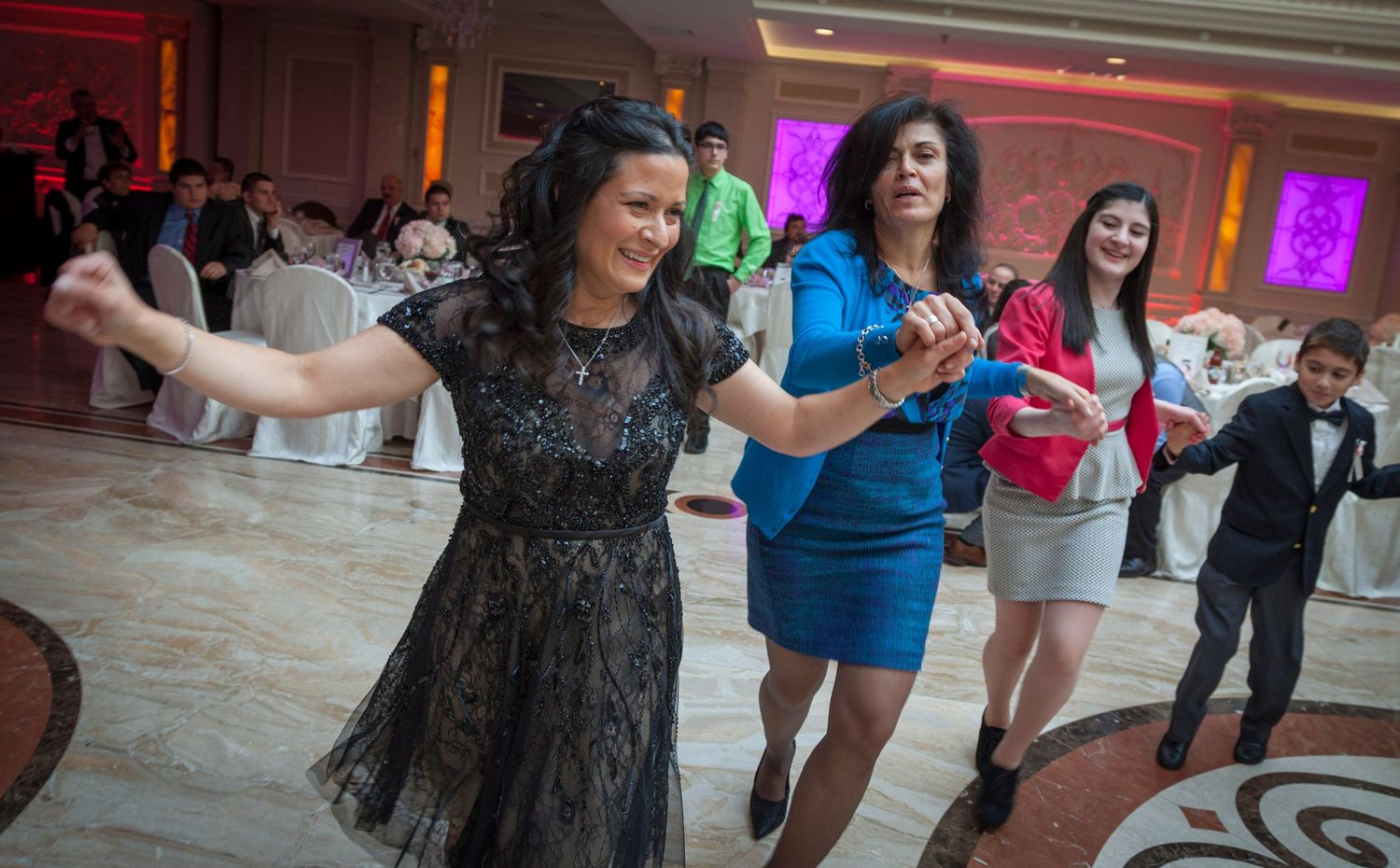 Women dancing joyfully at an elegant wedding reception in a ballroom with guests in the background.