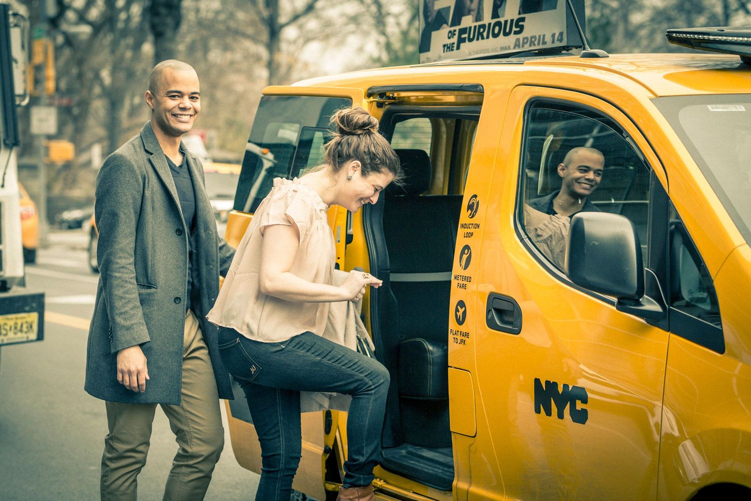 A woman steps out of a yellow NYC taxi cab while two people smile nearby on a tree-lined street.