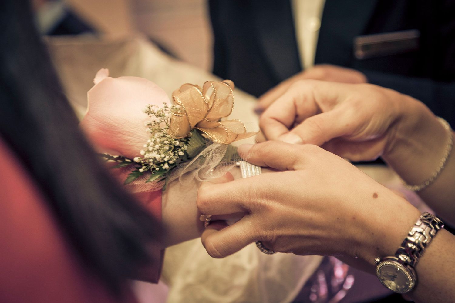 Close-up of a groom placing a wedding ring on the bride's finger, with a pink rose corsage visible.