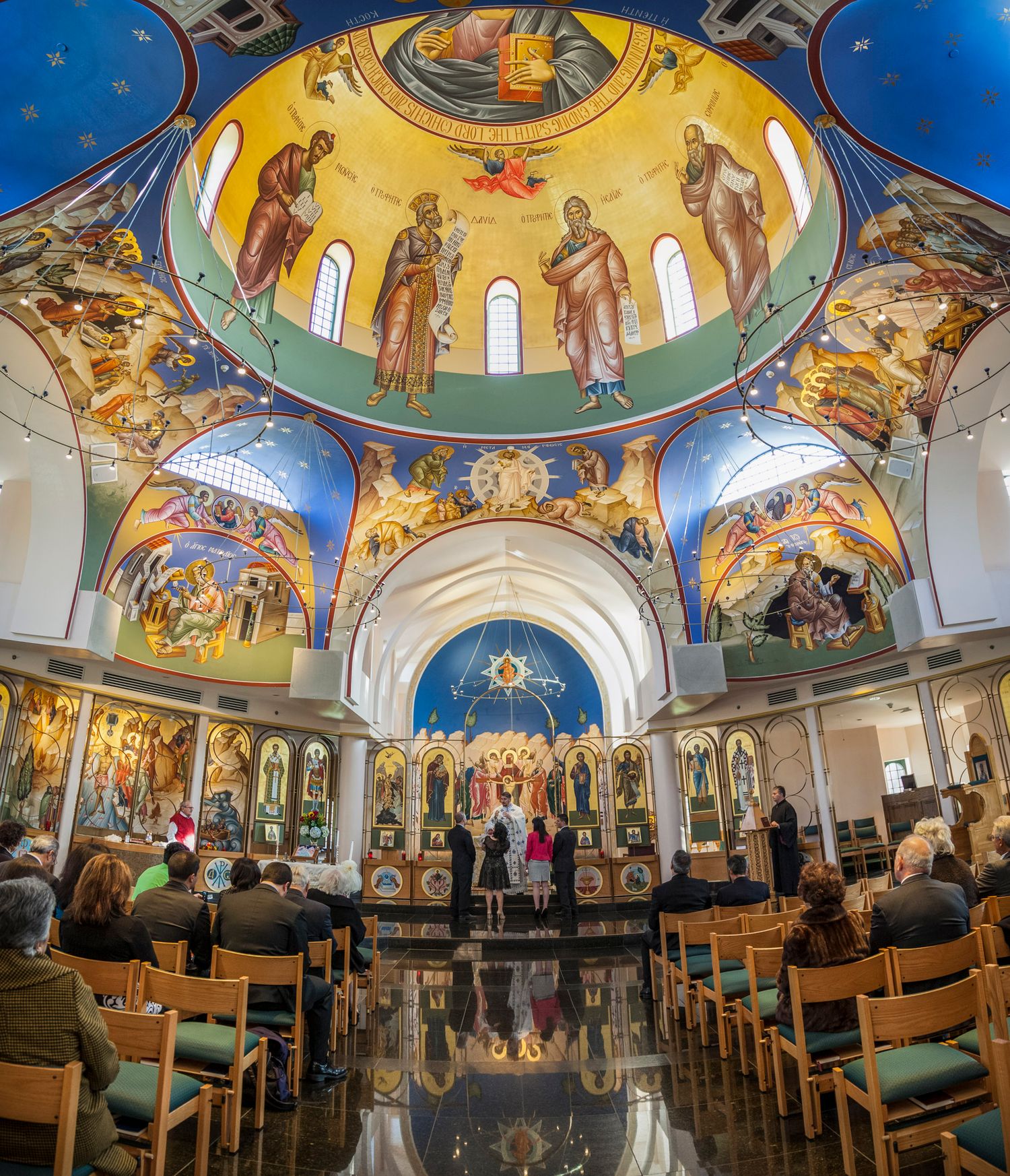 Stunning Orthodox church interior with ornate dome ceiling murals and golden iconostasis during a ceremony.