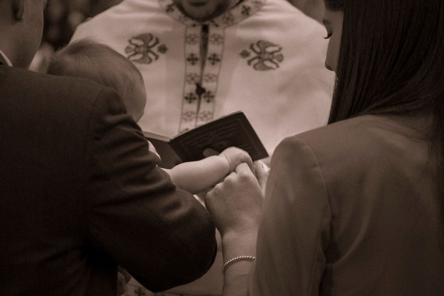 Couple holding a Bible during a religious ceremony with a priest in embroidered vestments in the background.