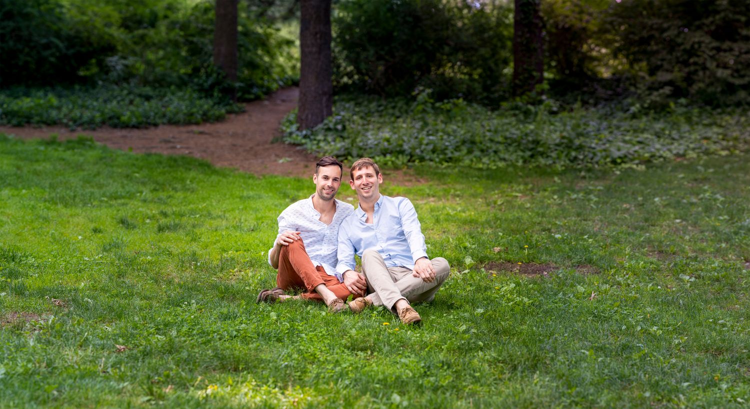 Happy couple sitting together on lush green grass in a park, smiling and enjoying a sunny day outdoors.
