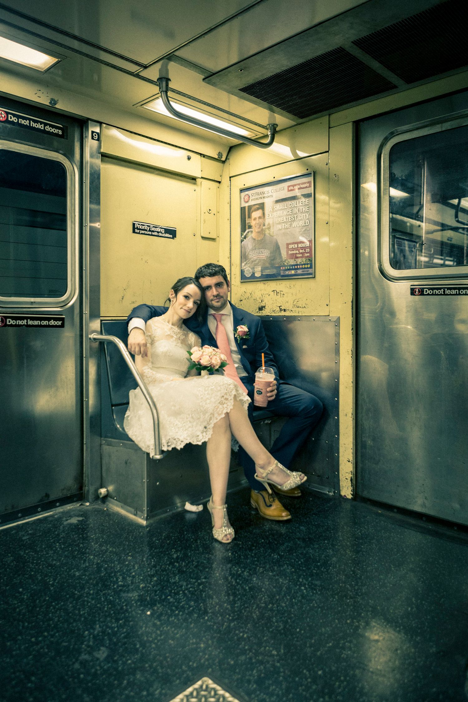 Newlyweds sitting together on a vintage NYC subway car in wedding attire, groom holding a drink.
